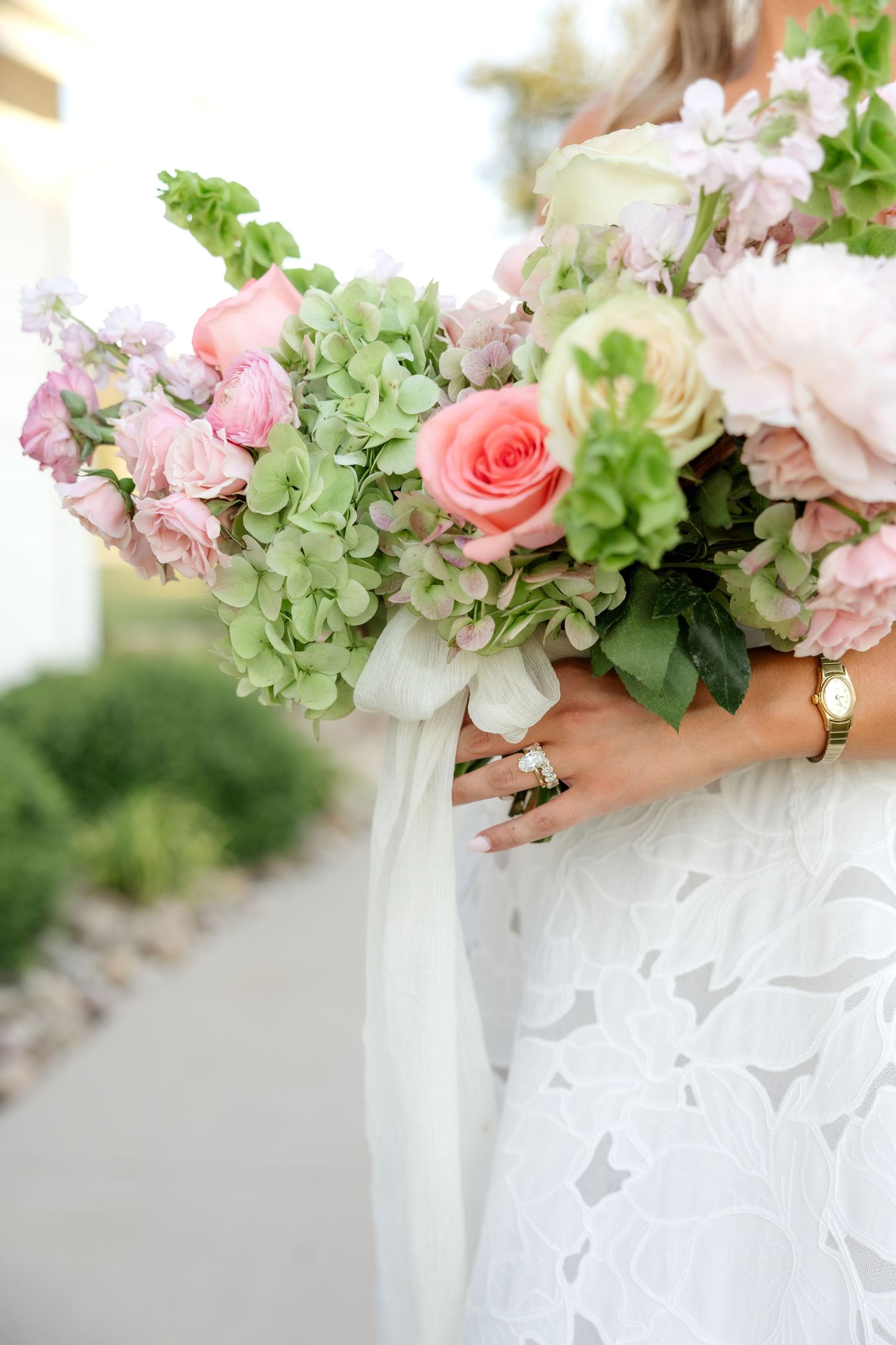 Close-up of a bride wearing floral lace wedding dress and diamond engagement ring and wedding band, holding lush pastel bridal bouquet