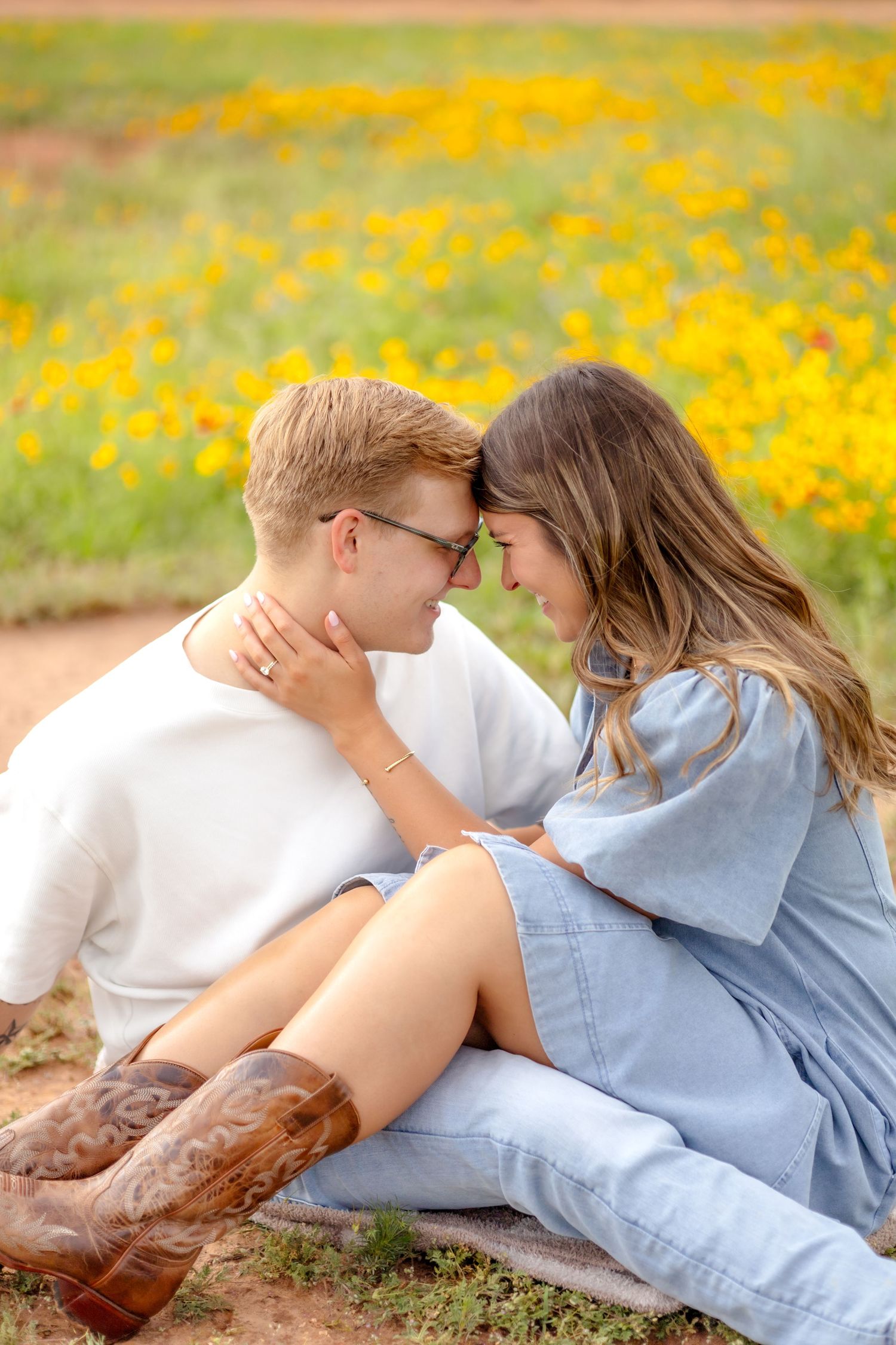 Wife sitting with her husband in a flower field and resting their foreheads together during couple's photo session in Abilene, TX