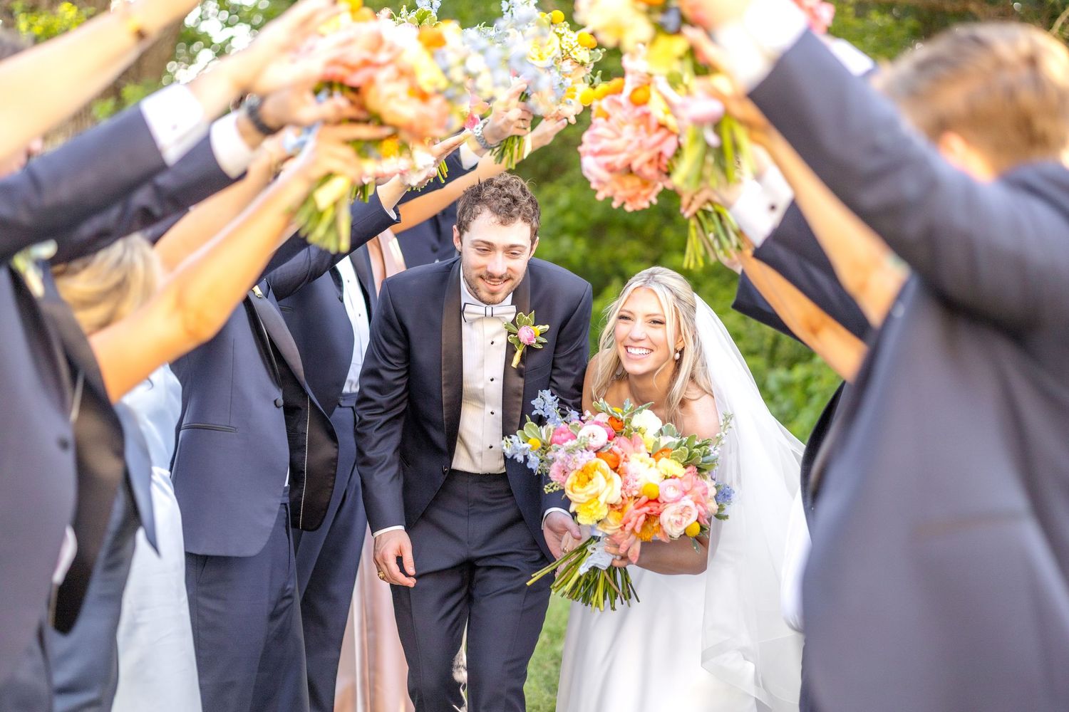 Bride and groom running together through the tunnel their wedding party made