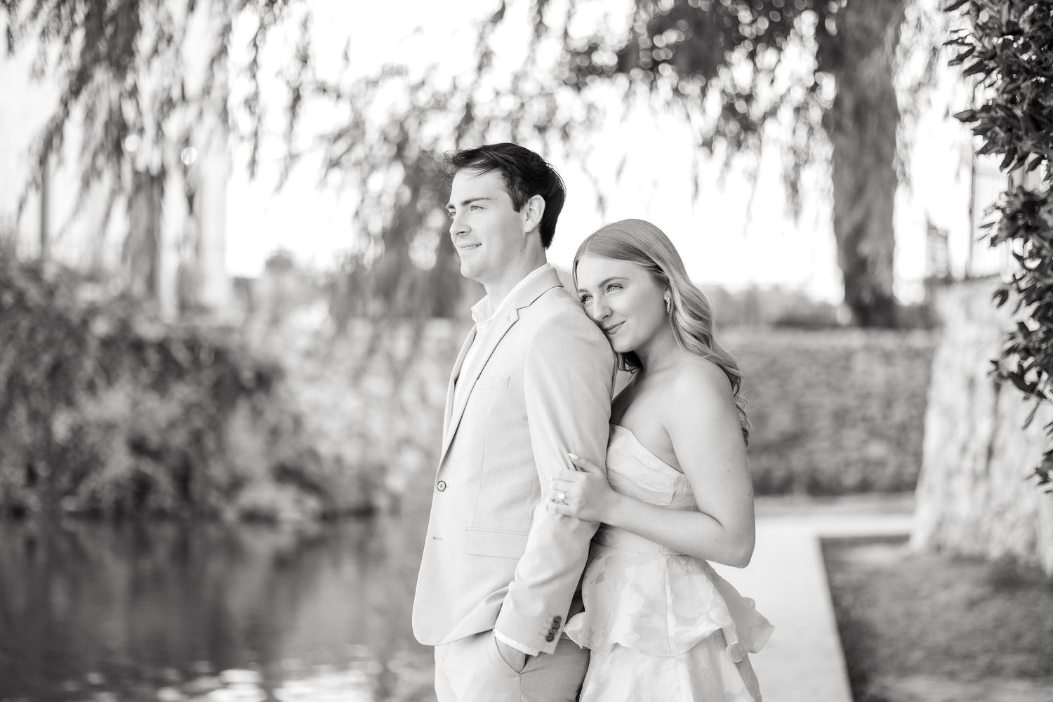 Engaged woman resting her head on her fiancé's back and looking out in distance at Dallas engagement session at Adriatica Village