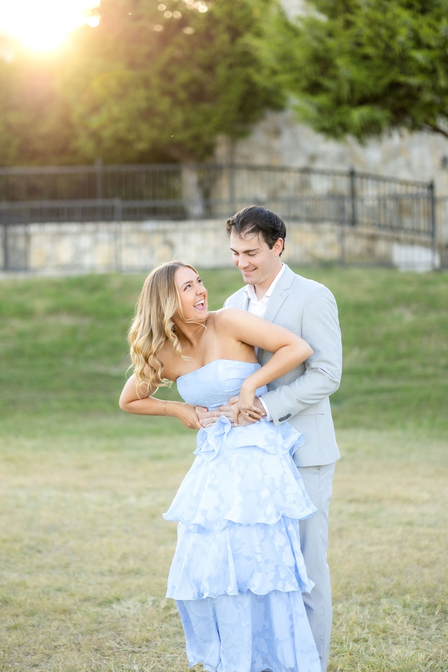Fiancees playing around in a field at Adriatica Village and laughing during Dallas engagement photo session