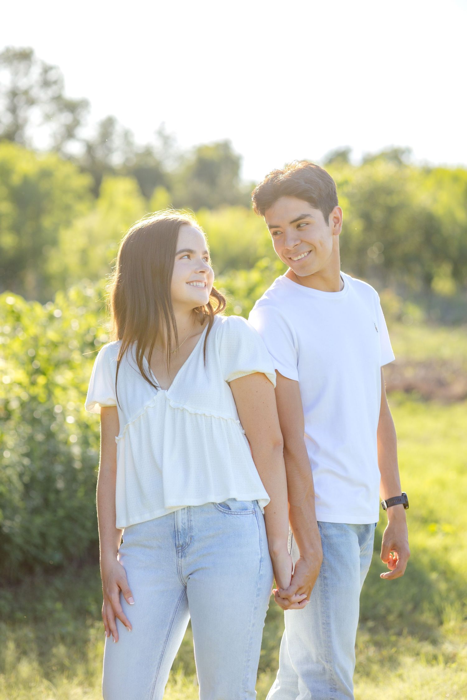 Engaged couple standing back to back and looking over their shoulder at one another at Dallas engagement session