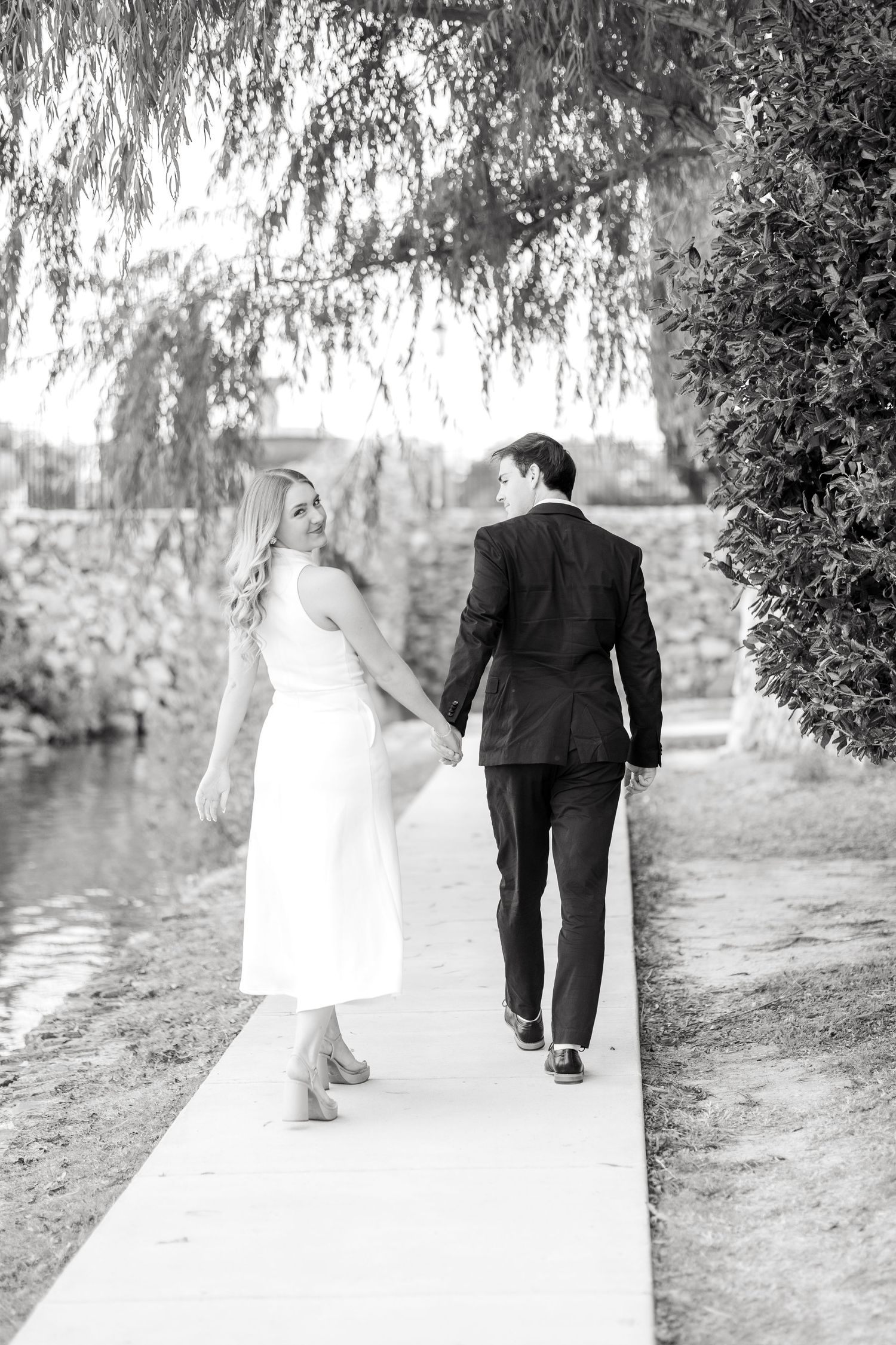 Engaged couple walking away hand in hand as the bride looks back and smiles at Adriatica Village