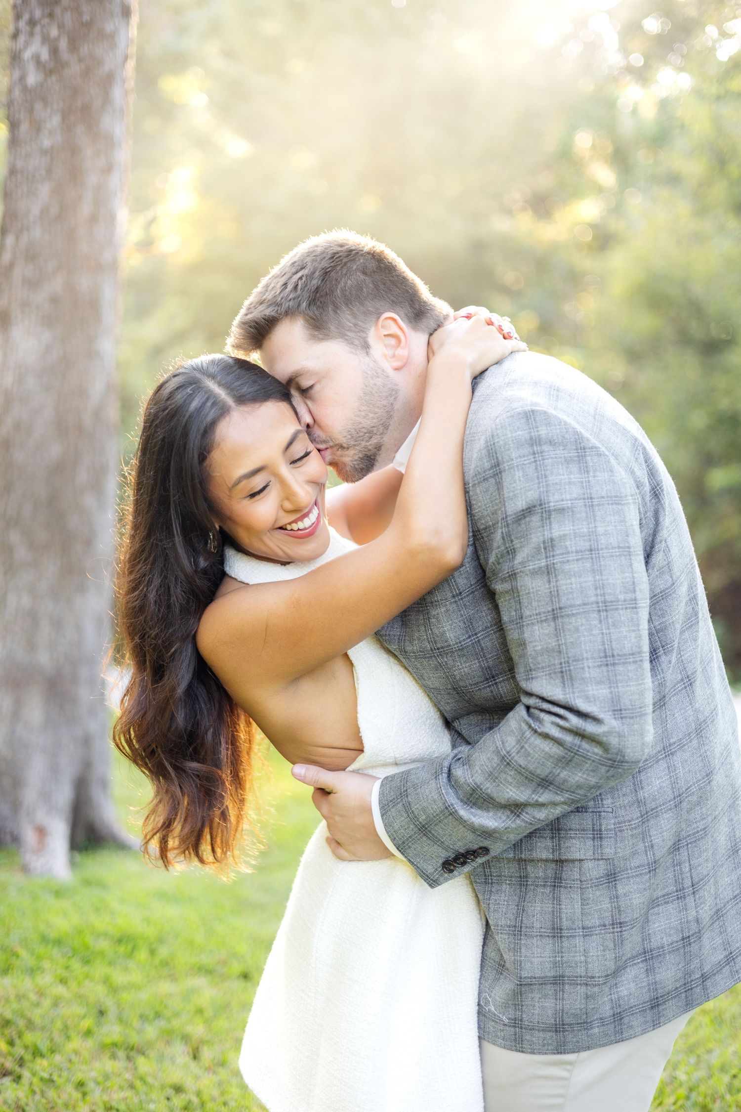 Engaged couple leaning back and kissing on the cheek in golden hour light at Dallas, Texas engagement photo session at Lakeside Park