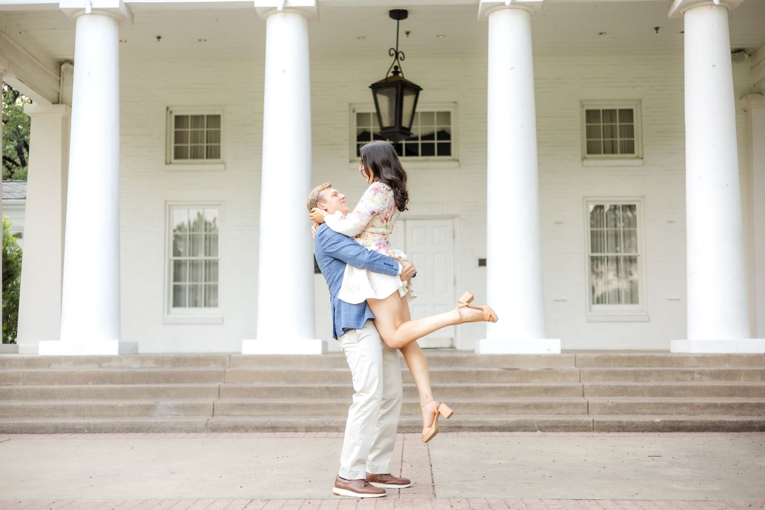 Engaged couple doing a princess lift in front of a beautiful white event venue with tall pillars