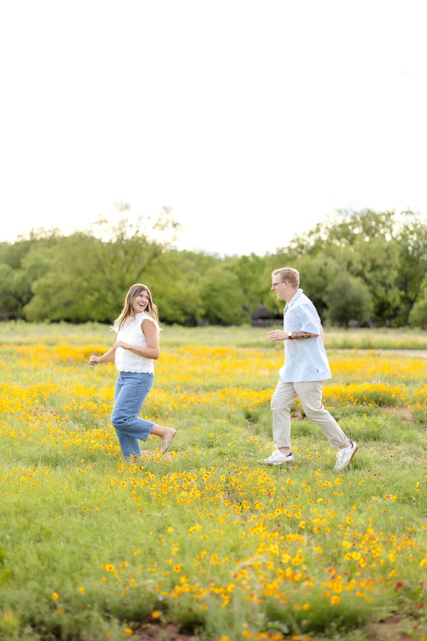 Husband and wife running together through a field full of yellow wildflowers during couple's photo session in Abilene, TX