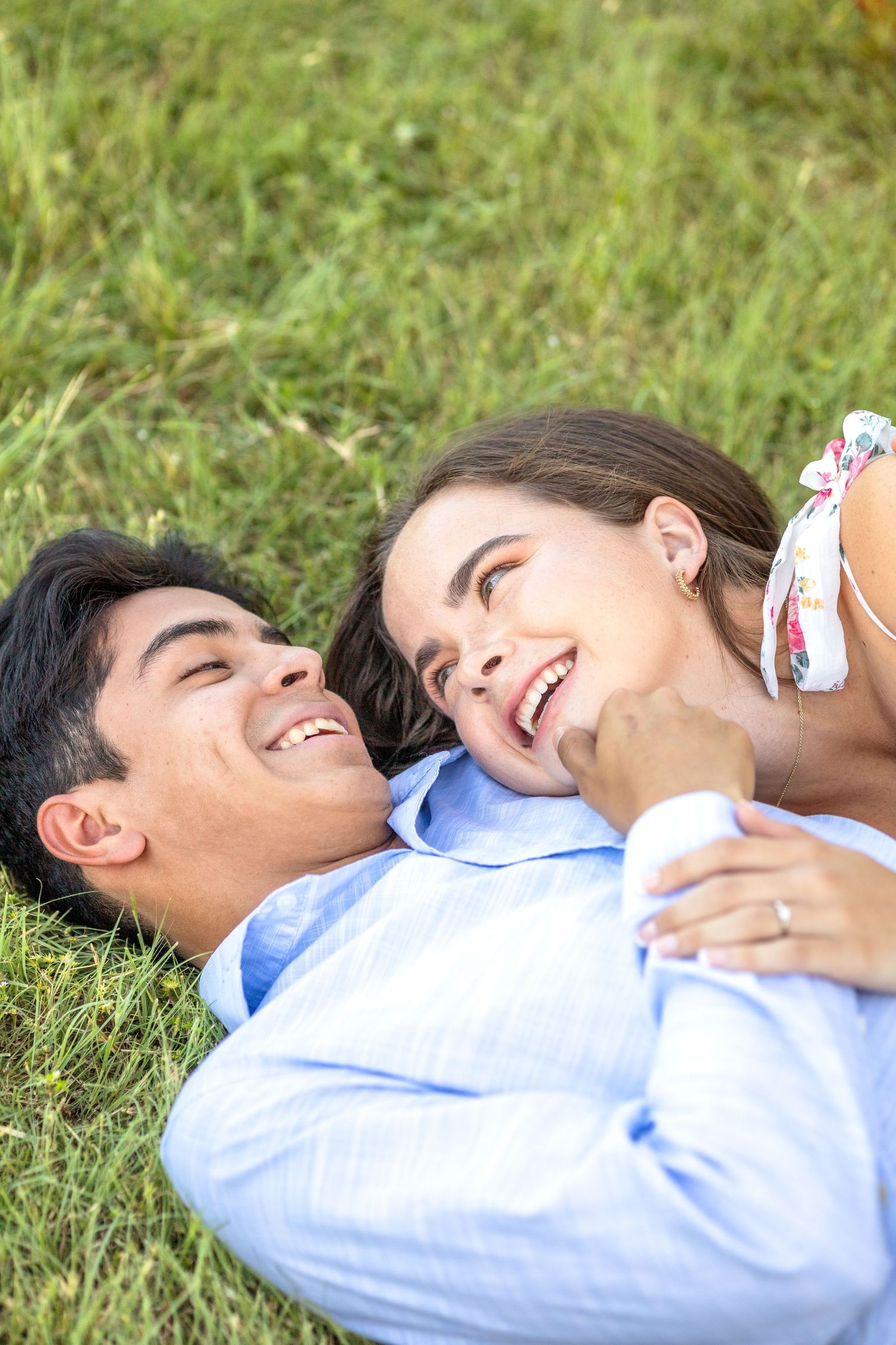 Engaged couple laying in the grass at White Rock Lake and smiling at one another