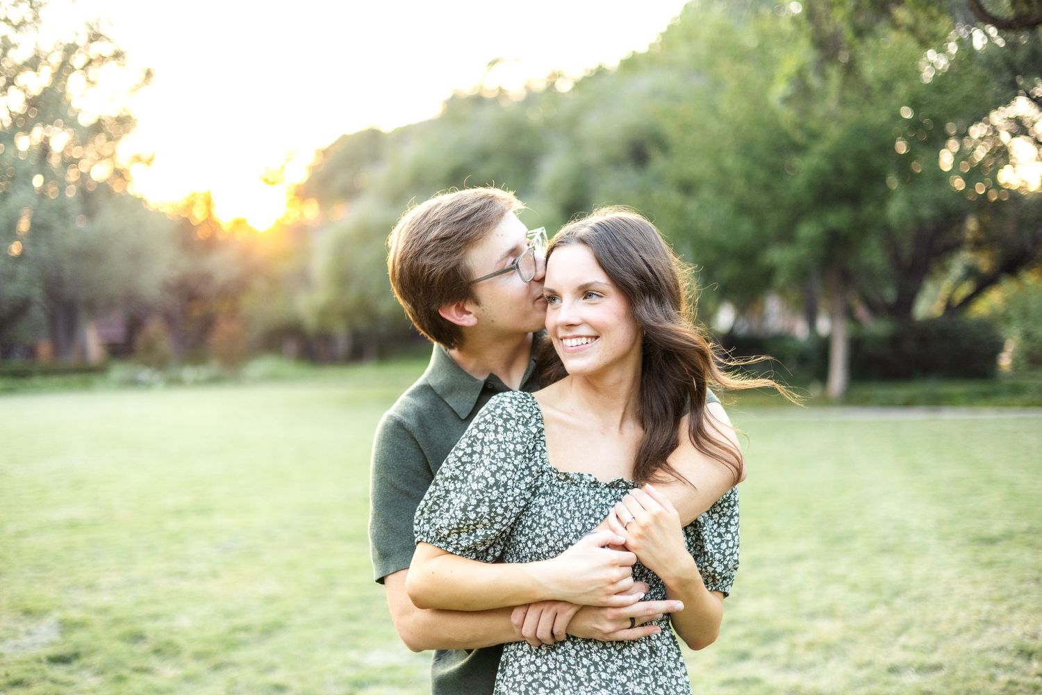 Engaged man hugging his fiancé and whispering into her ear during golden hour light at Flippen Park in Dallas, TX engagement session