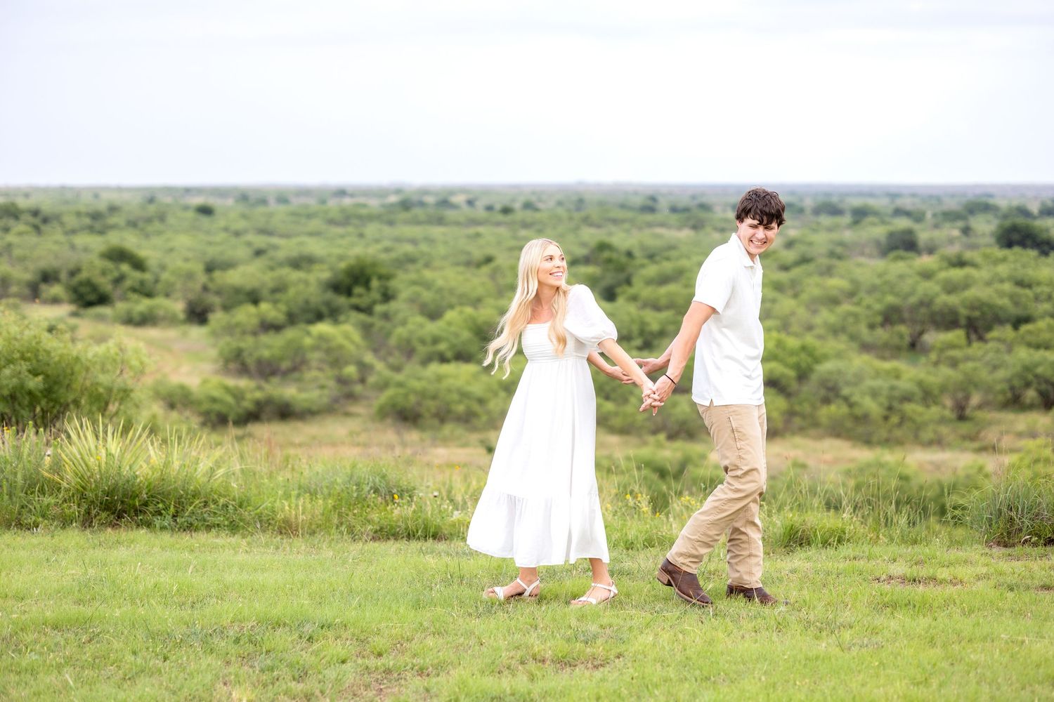 Engaged couple holding hands back to back and stepping in and out while laughing
