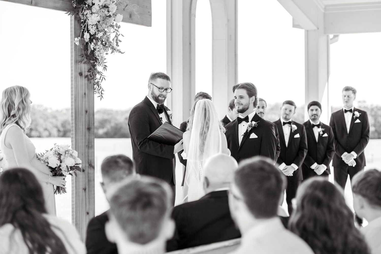 Black and white image of groom smiling at the bride during wedding ceremony at Chandelier Farms near Dallas, Texas