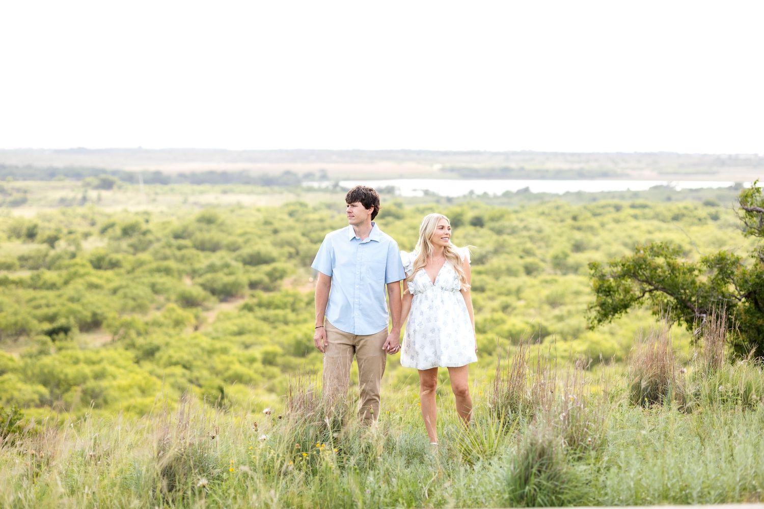 Engaged couple smiling and glancing off in different directions on a beautiful ranch in Texas during engagement photo session.