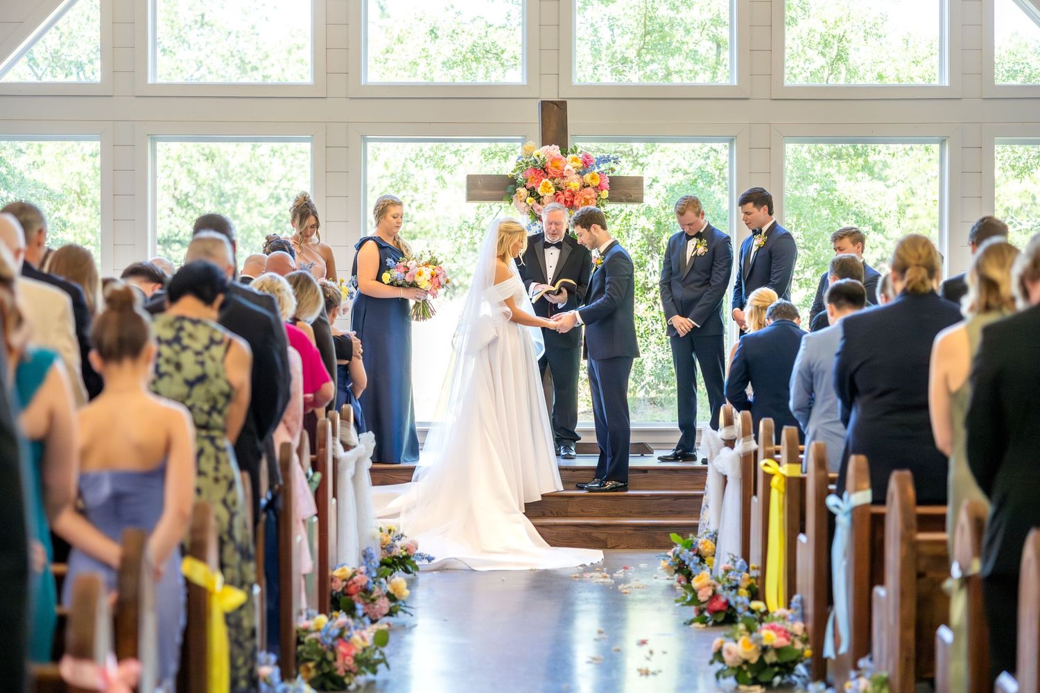 Aisle shot of bride and groom holding hands during their wedding ceremony and praying together at Dallas wedding