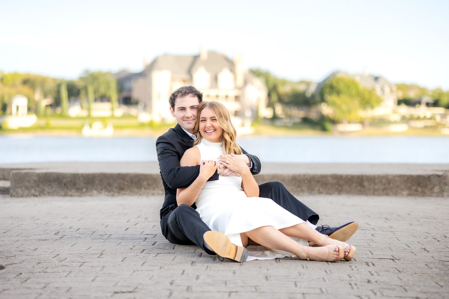 Engaged couple sitting cuddled up on the dock at Adriatica Village looking out over a beautiful lake at Dallas engagement photo session