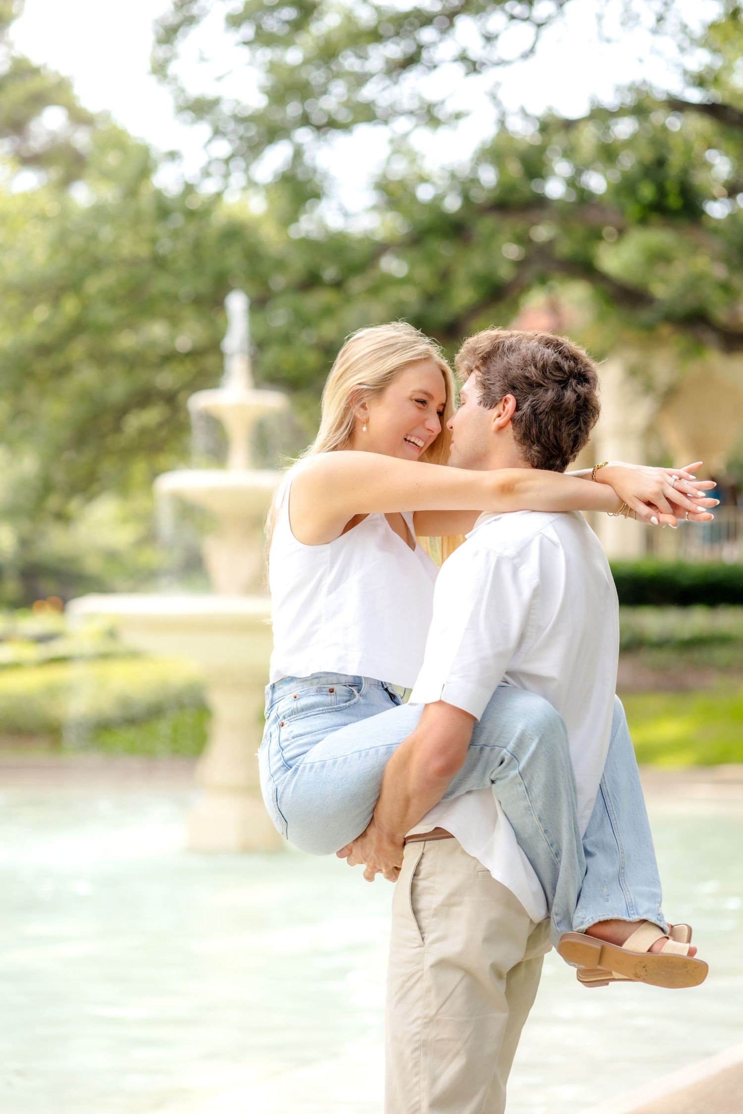 Engaged couple lifting up the girl and resting their heads together in front of the fountain at Flippen Park in Dallas