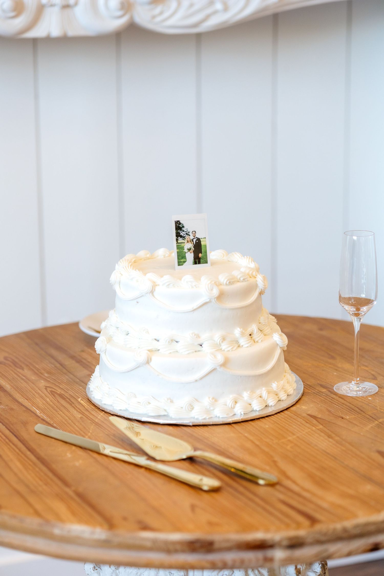 White wedding cake sitting on table at Dallas wedding reception with a polaroid photo of the bride and groom as the cake topper