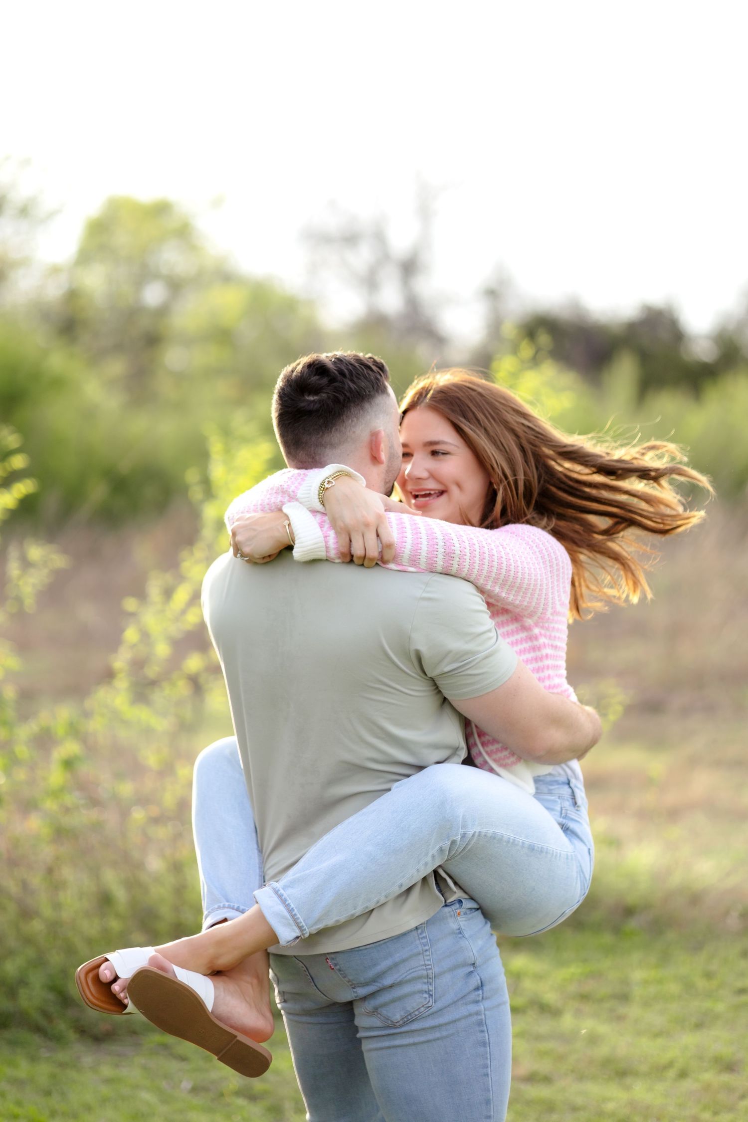 Engaged couple spinning around in a field and laughing with one another in Dallas, Texas at their engagement photo session