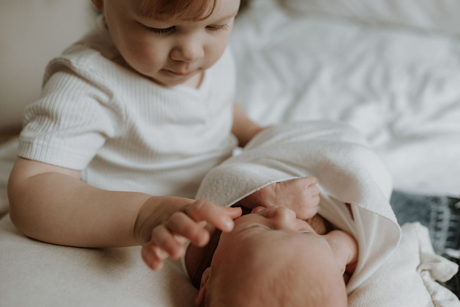 Adorable sleeping baby in cozy Edmonton studio setup, perfect example of newborn photography with soft lighting with sibling interaction.