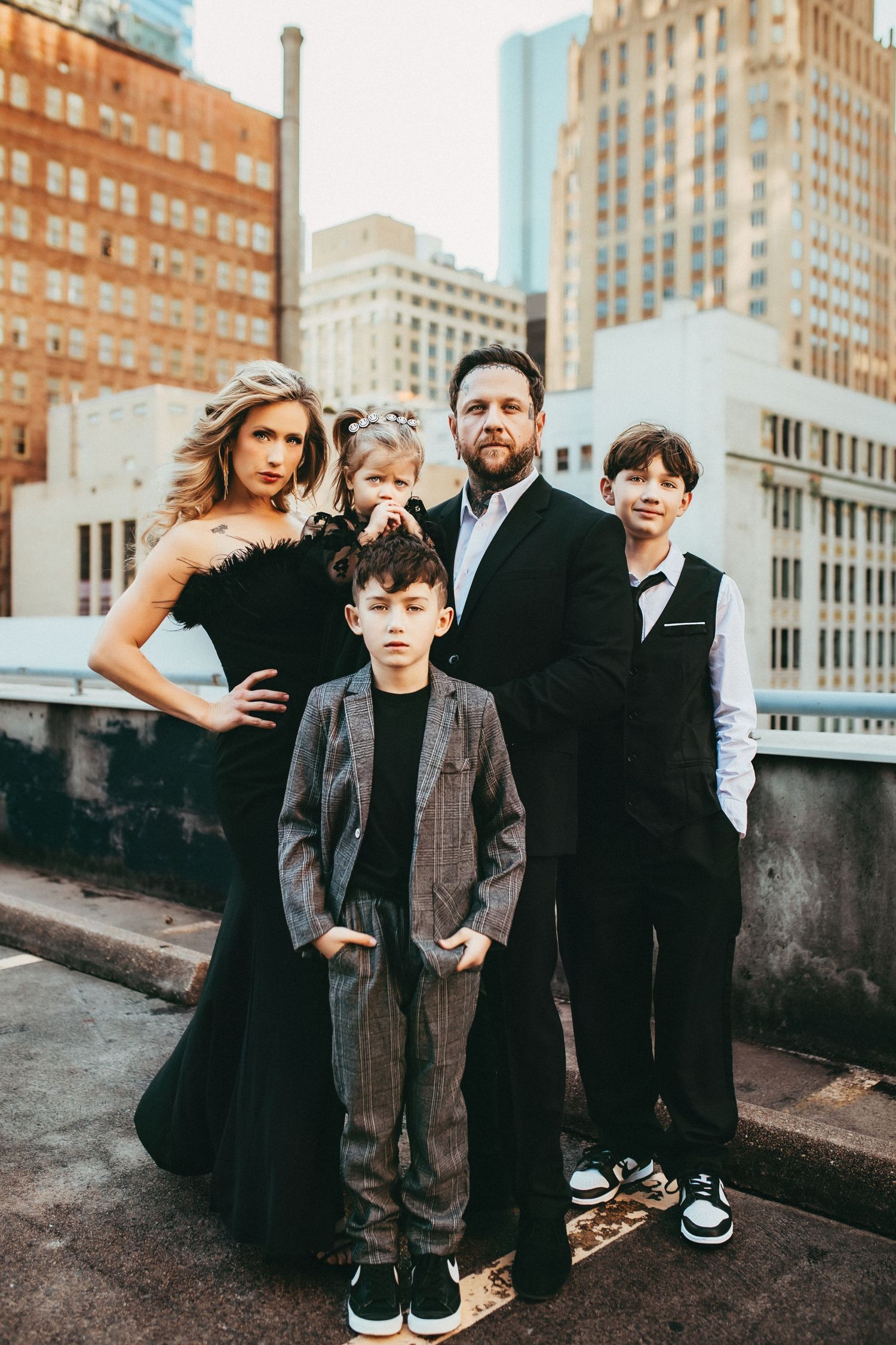 Family group in formal attire poses together on city rooftop with urban skyline backdrop.