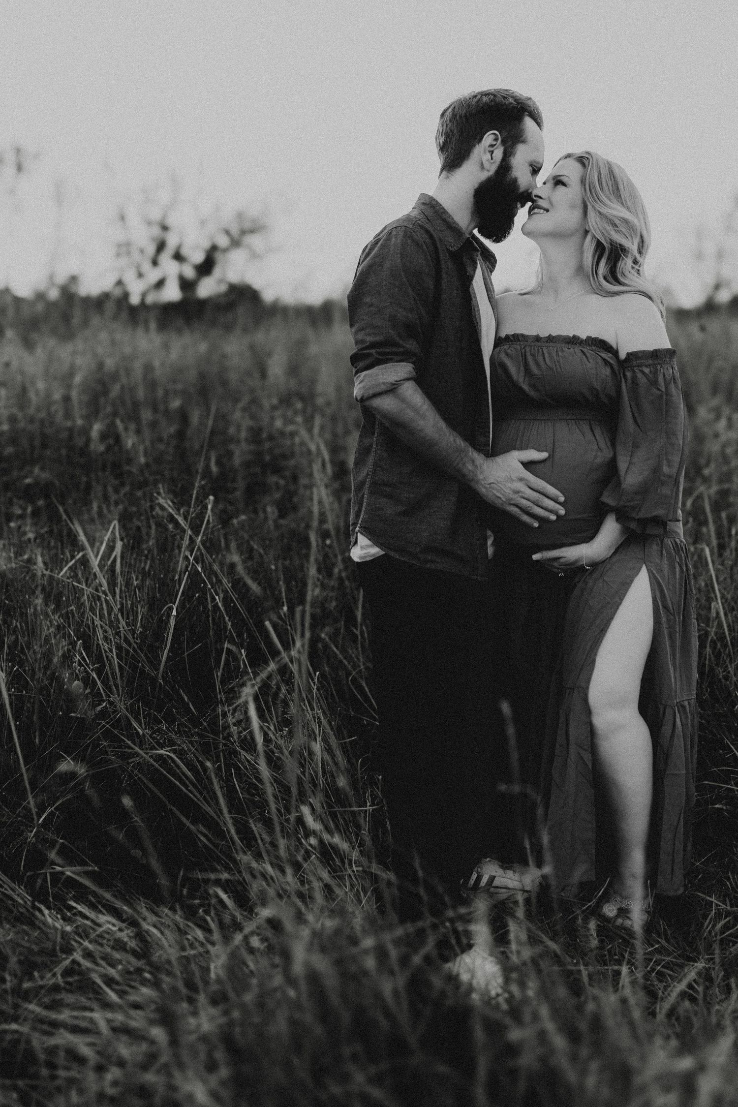 A couple embraces in a peaceful outdoor setting with tall grasses during an intimate black and white photo session.