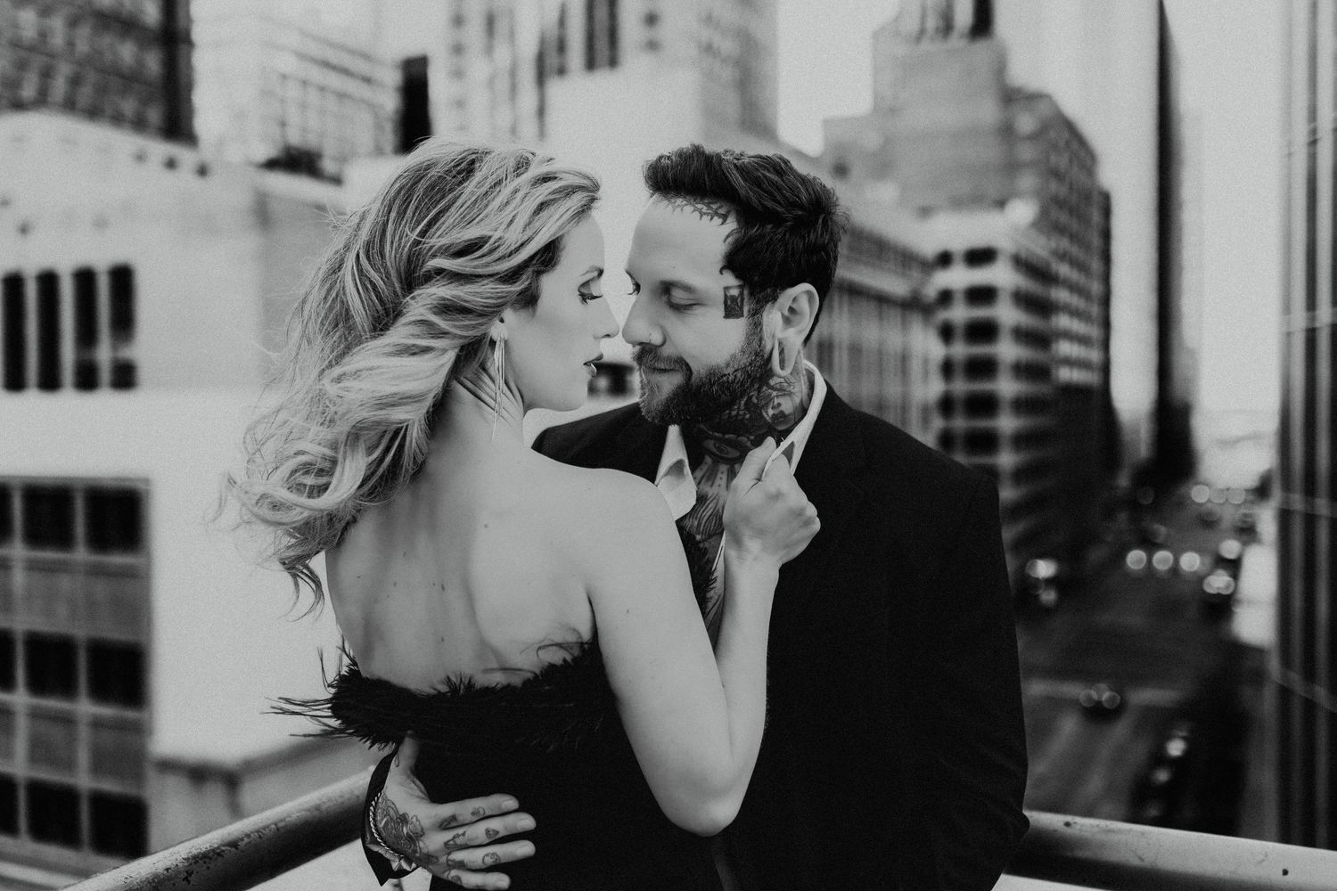 Black and white photo captures intimate moment between couple on urban rooftop with dramatic architecture.