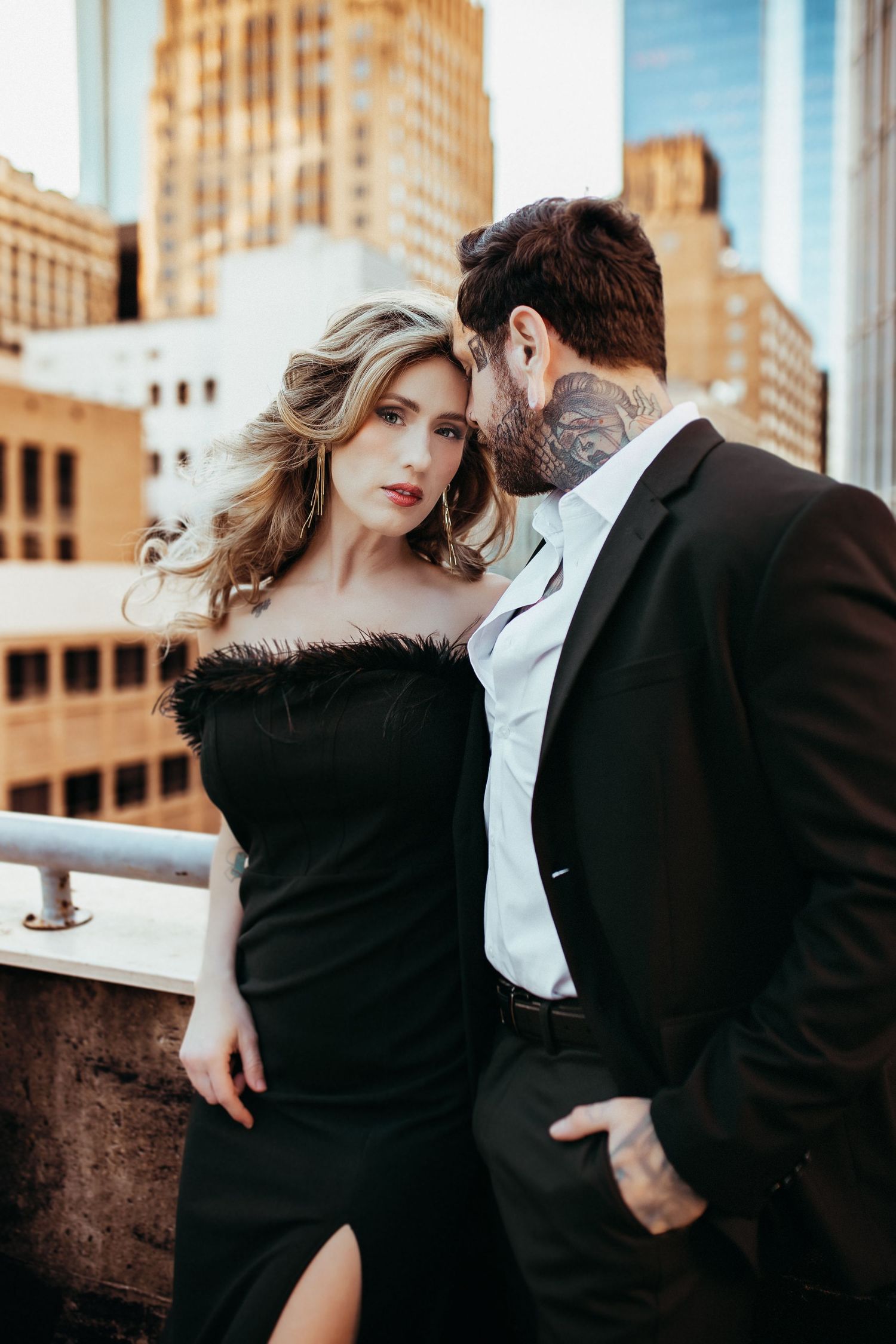 Stylish couple poses intimately on urban rooftop with city buildings in background during sunset photoshoot.