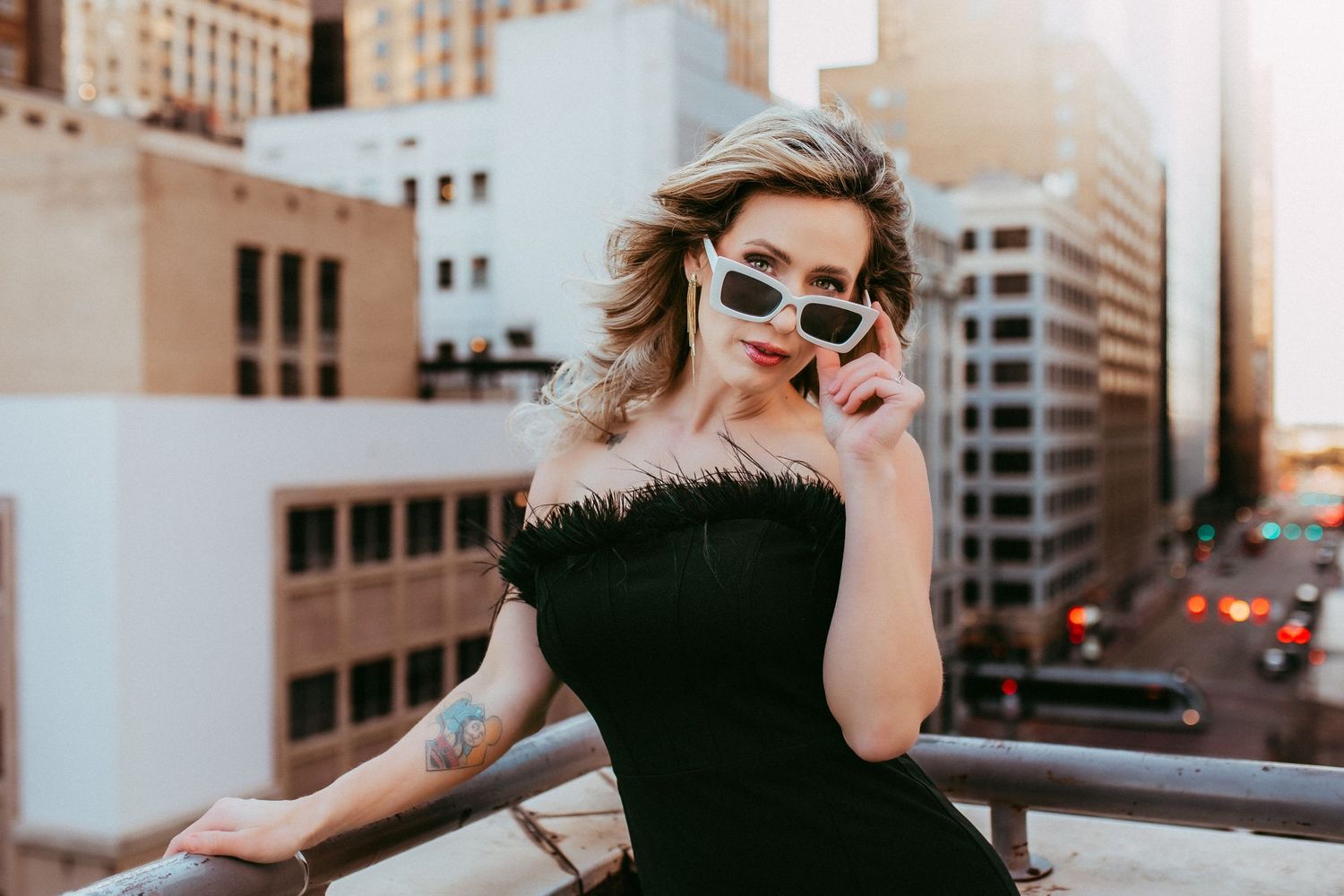 Couple in sunglasses poses on rooftop with vintage architectural elements and city skyline.