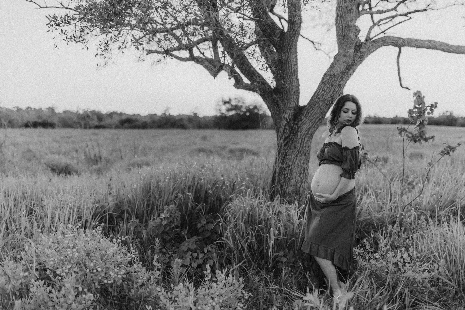 A vintage black and white photograph of a figure standing beside a lone tree in a grassy rural landscape.