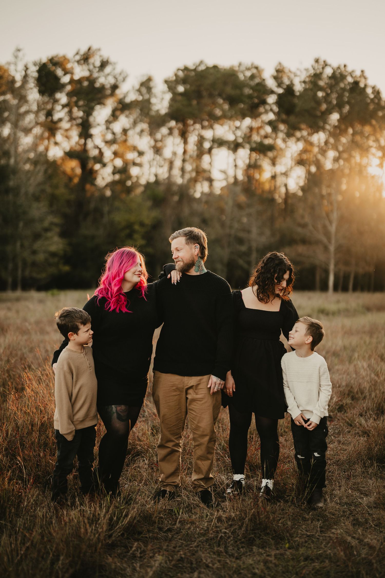 Modern family portrait of five people standing together in a sun-lit field during autumn.