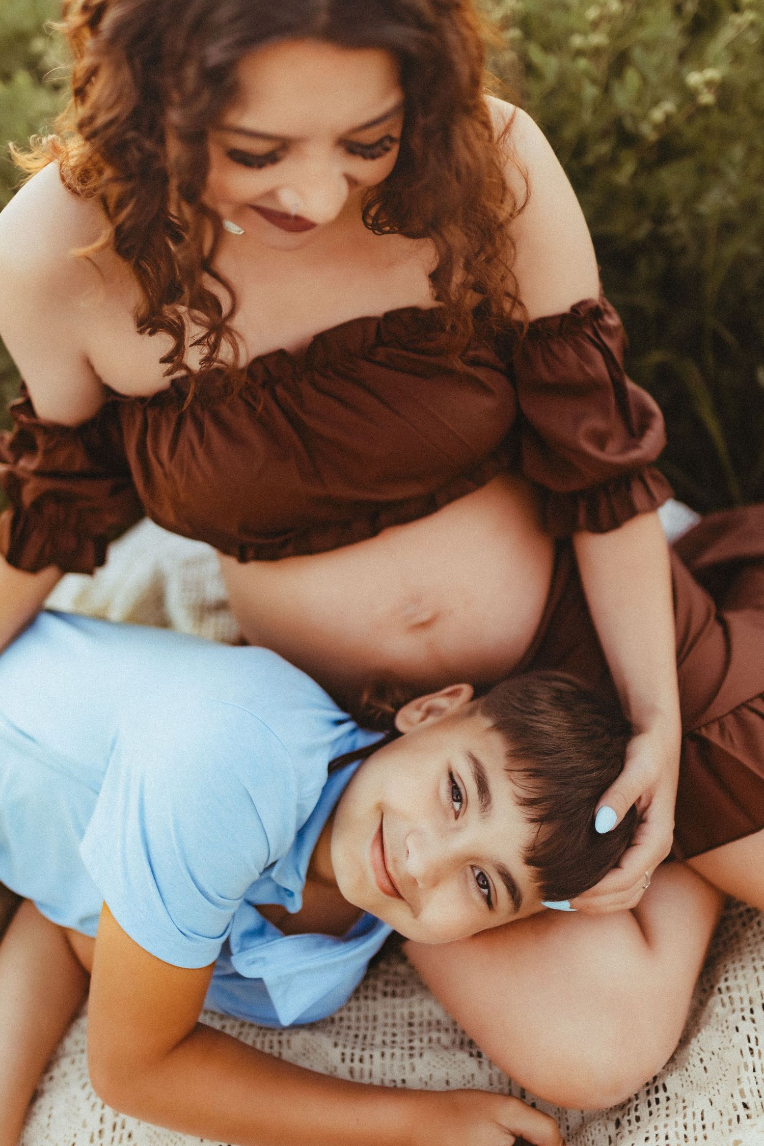 A woman in a brown dress embraces a young child in a blue shirt during an intimate photography session.