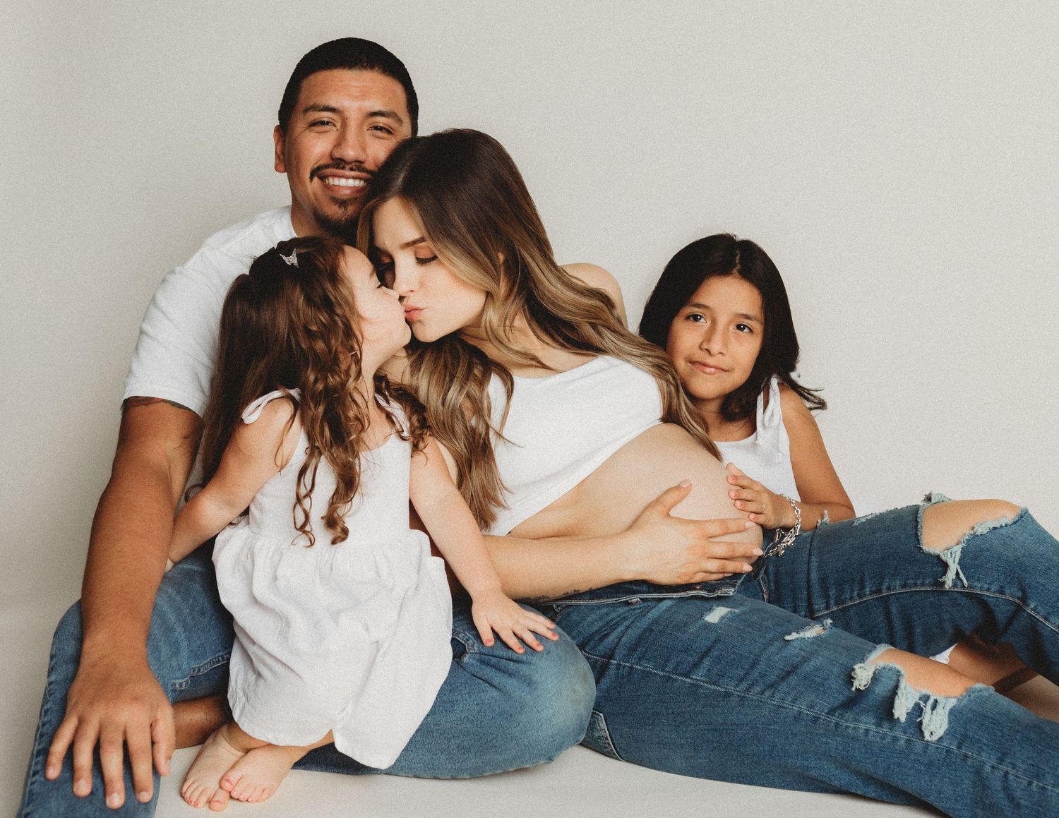 People wearing white tops and blue jeans lie comfortably together on a white couch.