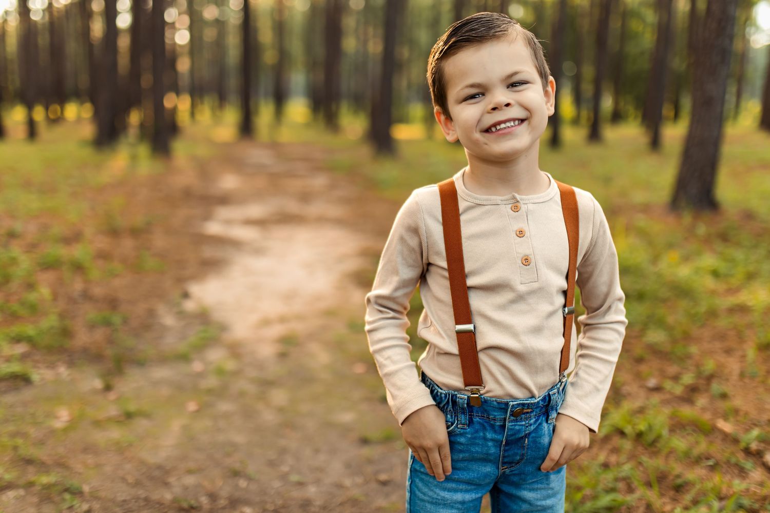 A young child wearing suspenders and a beige shirt walks along a forest path during autumn.
