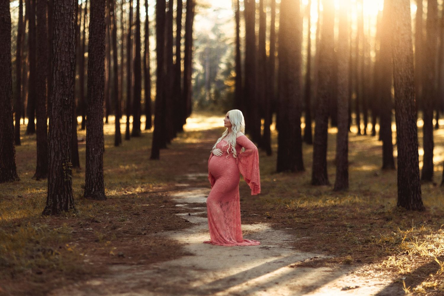 Golden sunlight streams through tall forest trees as a figure in flowing pink dress twirls among pine trunks.