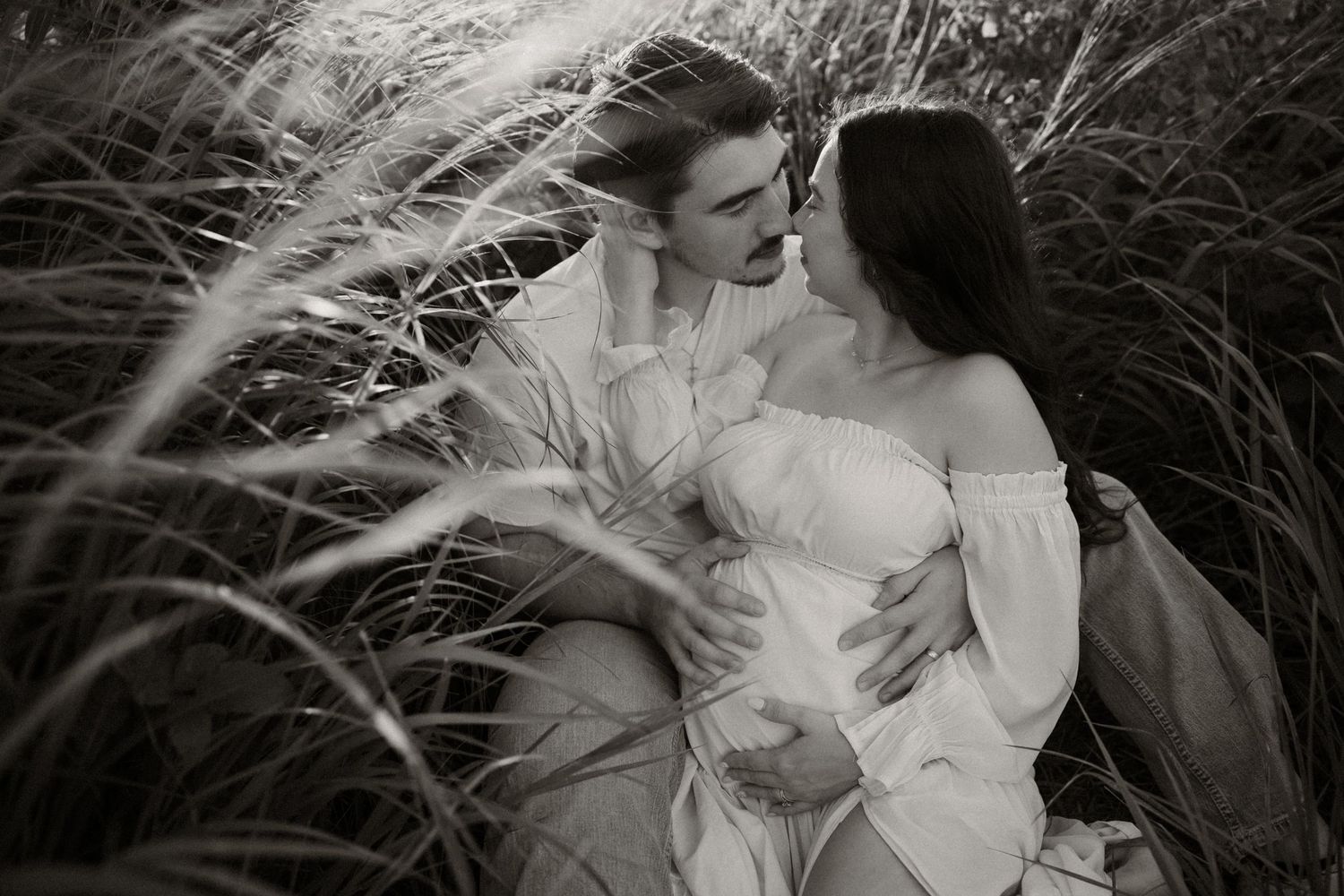A romantic black and white photo series showing a couple in vintage-style clothing embracing in tall grass.