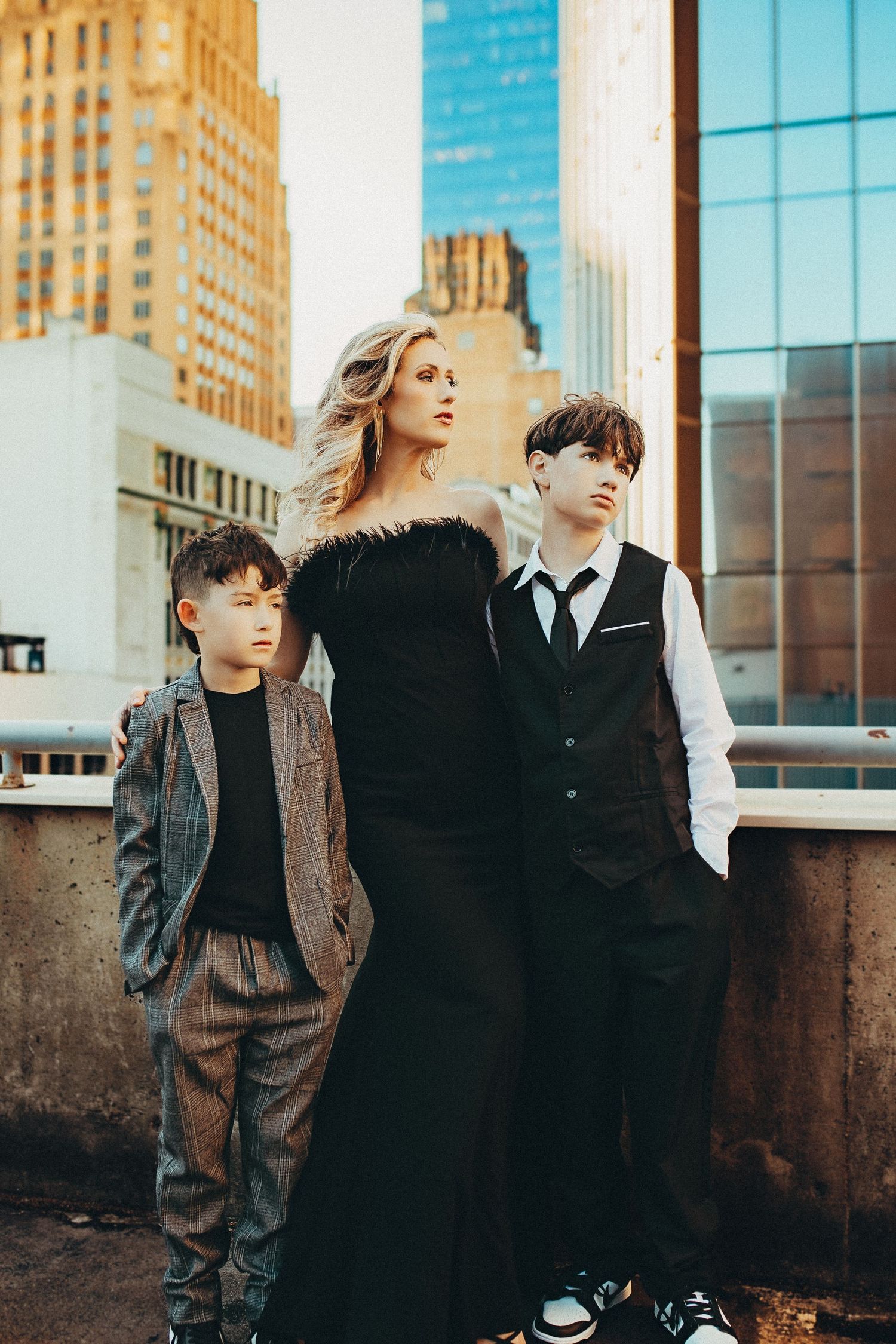 Family portrait of a woman in black gown with two children dressed formally against city skyline backdrop.