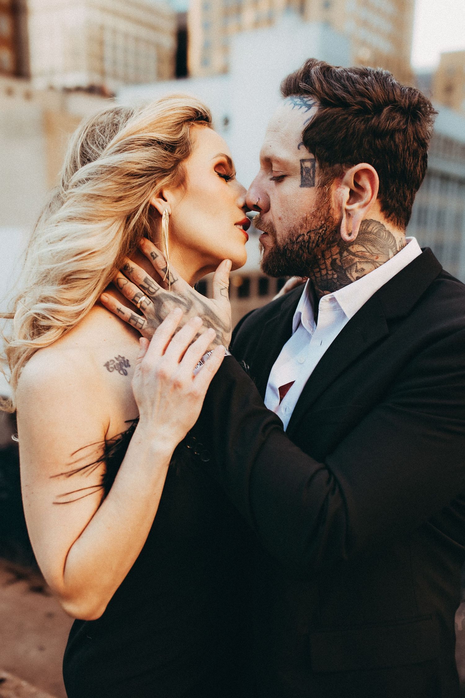Close-up shot of couple in black and white attire sharing tender moment on rooftop.