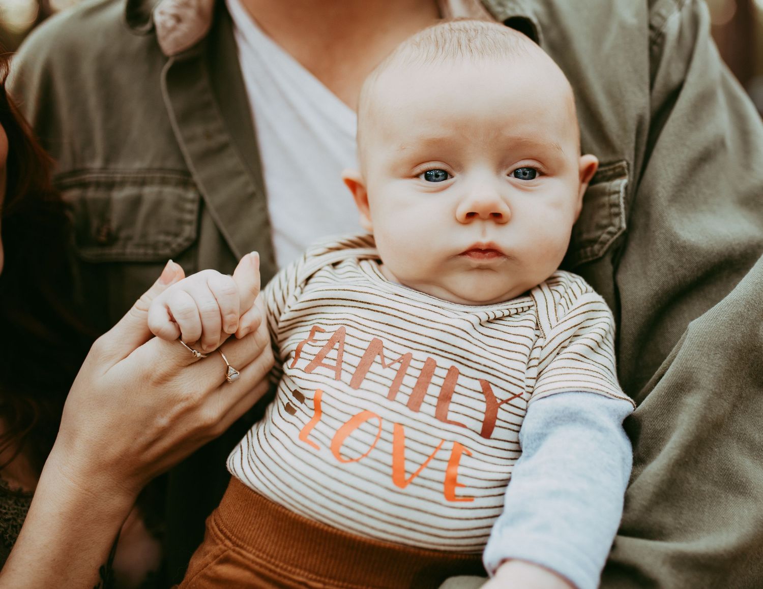 Close-up of an infant wearing a striped 'Family Love' shirt held by caring hands.