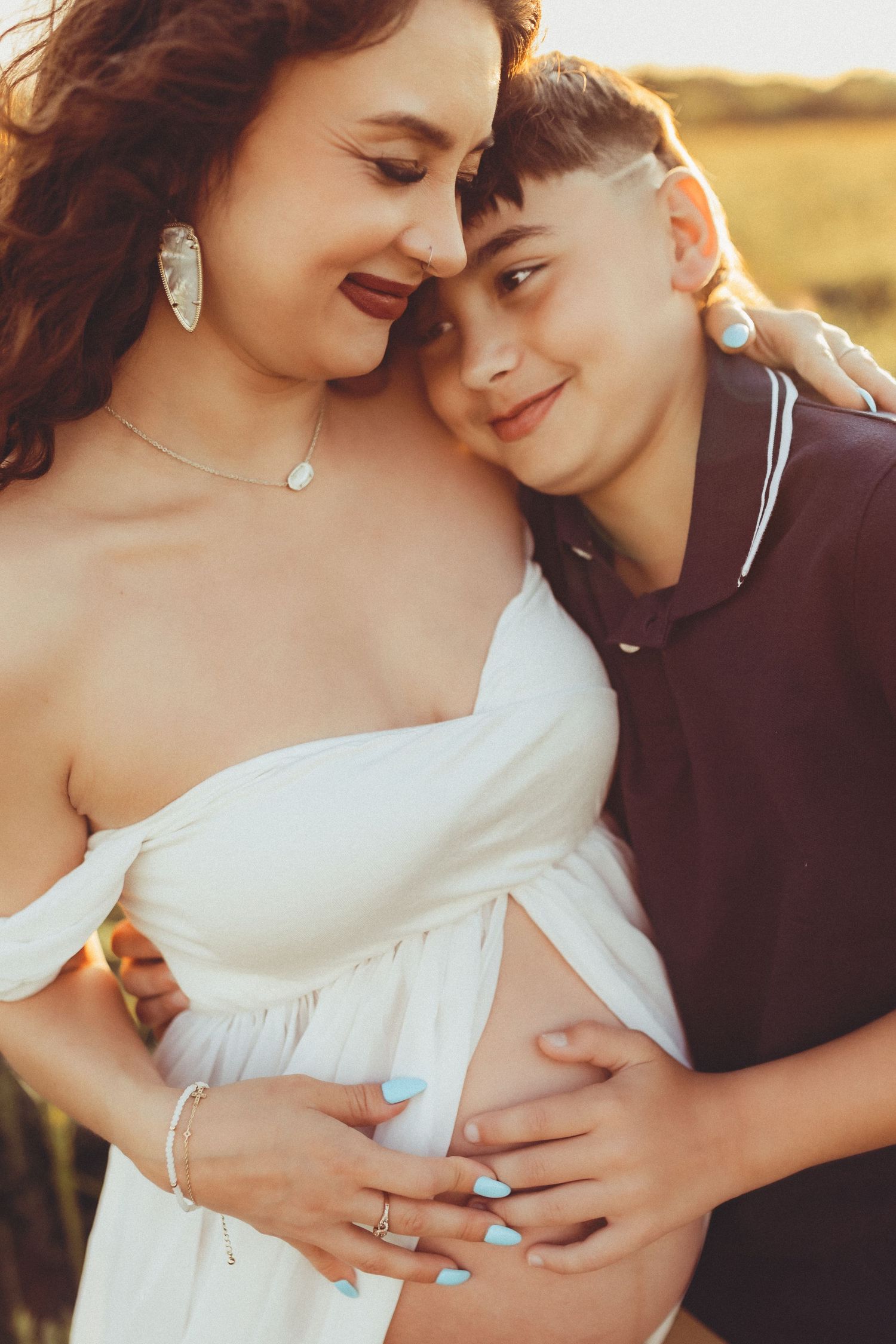 Intimate couple embraces outdoors at sunset, with focus on their hands gently touching a pregnant belly.