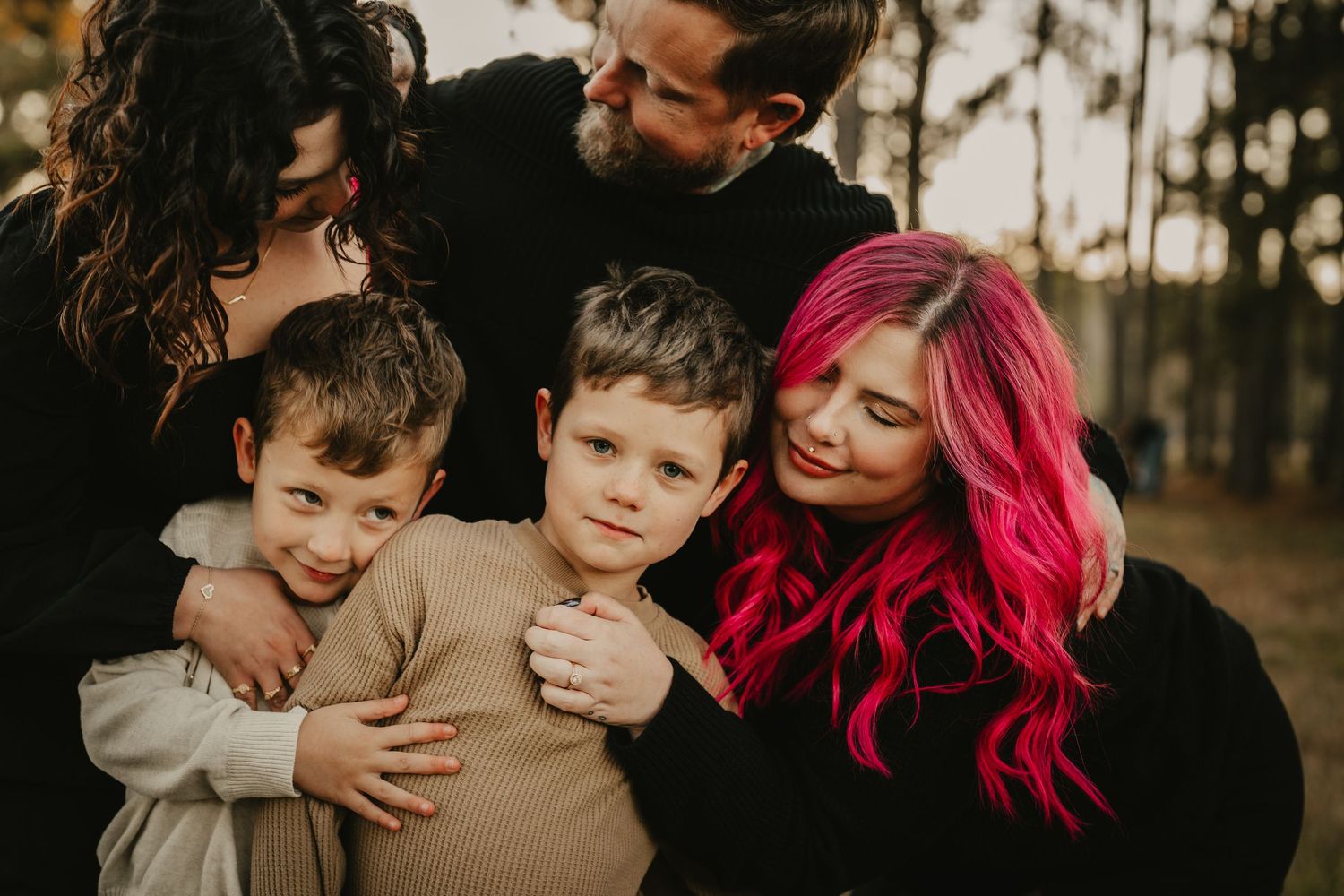 Candid family moment showing affection and laughter in a wooded setting.