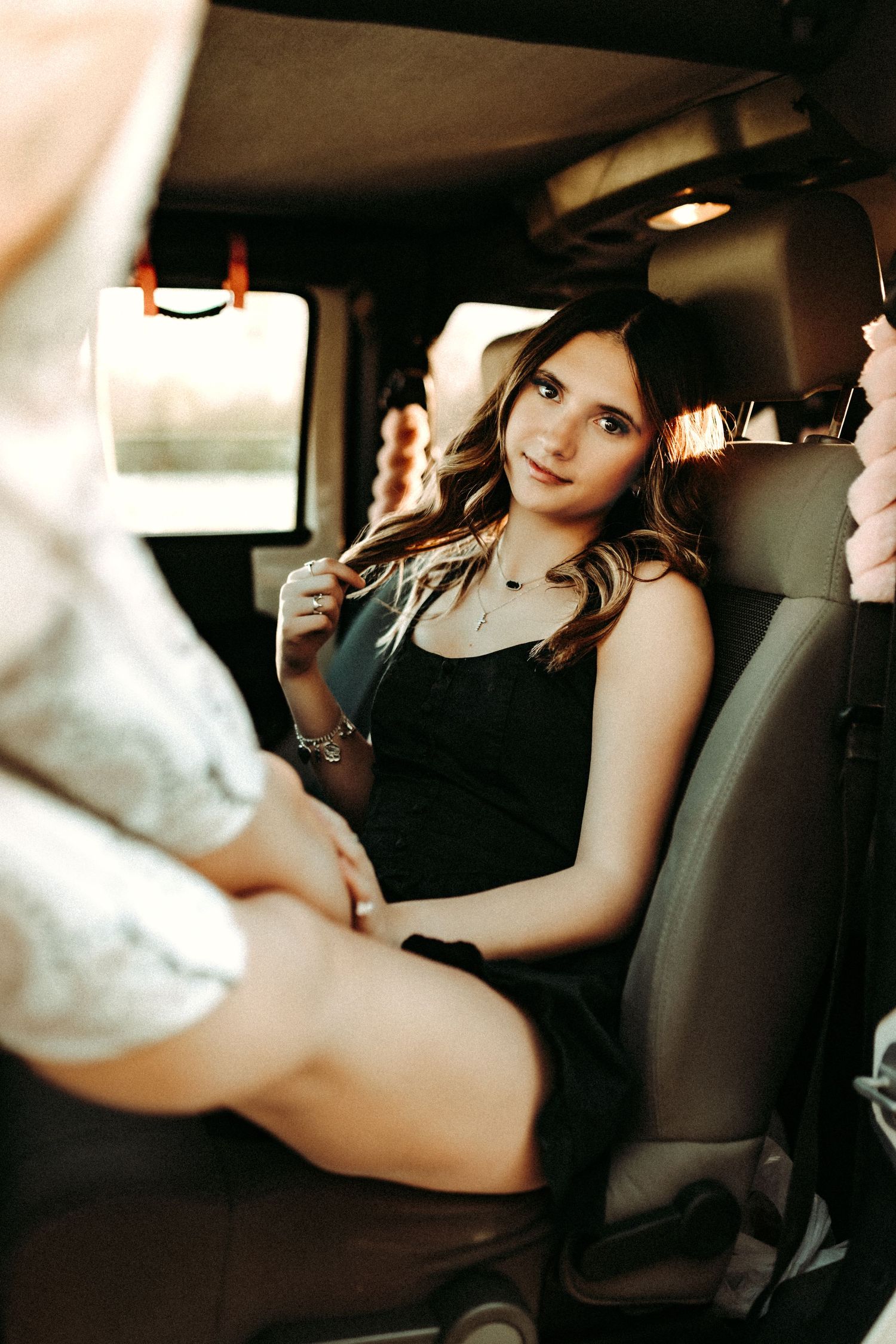 A person sits in the backseat of a car wearing a black tank top during a warm-toned photoshoot.