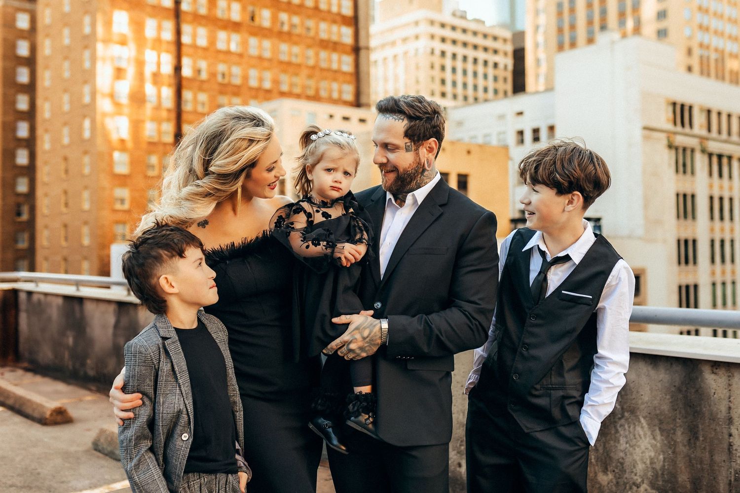 Elegant wedding couple and guests laughing together in urban setting against brick buildings and modern architecture.