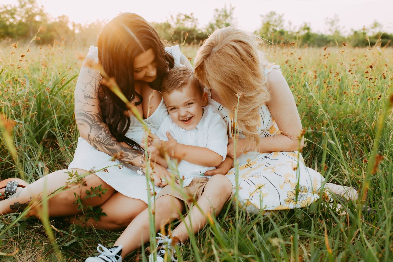 Three people sit together on grass in a wildflower meadow during golden hour sunlight.
