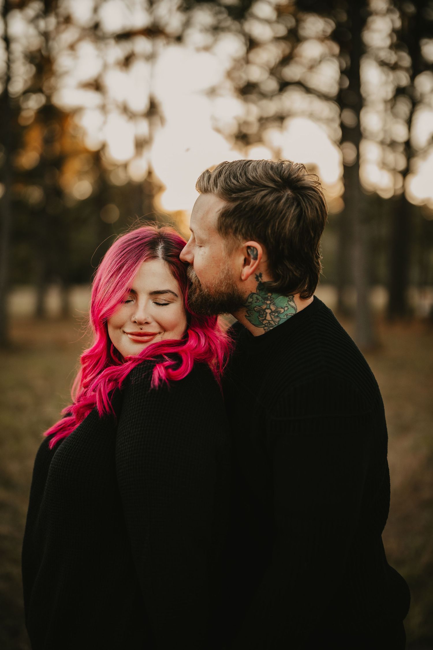 Intimate autumn sunset portrait of a couple with pink hair and tattoos sharing a tender moment in nature.