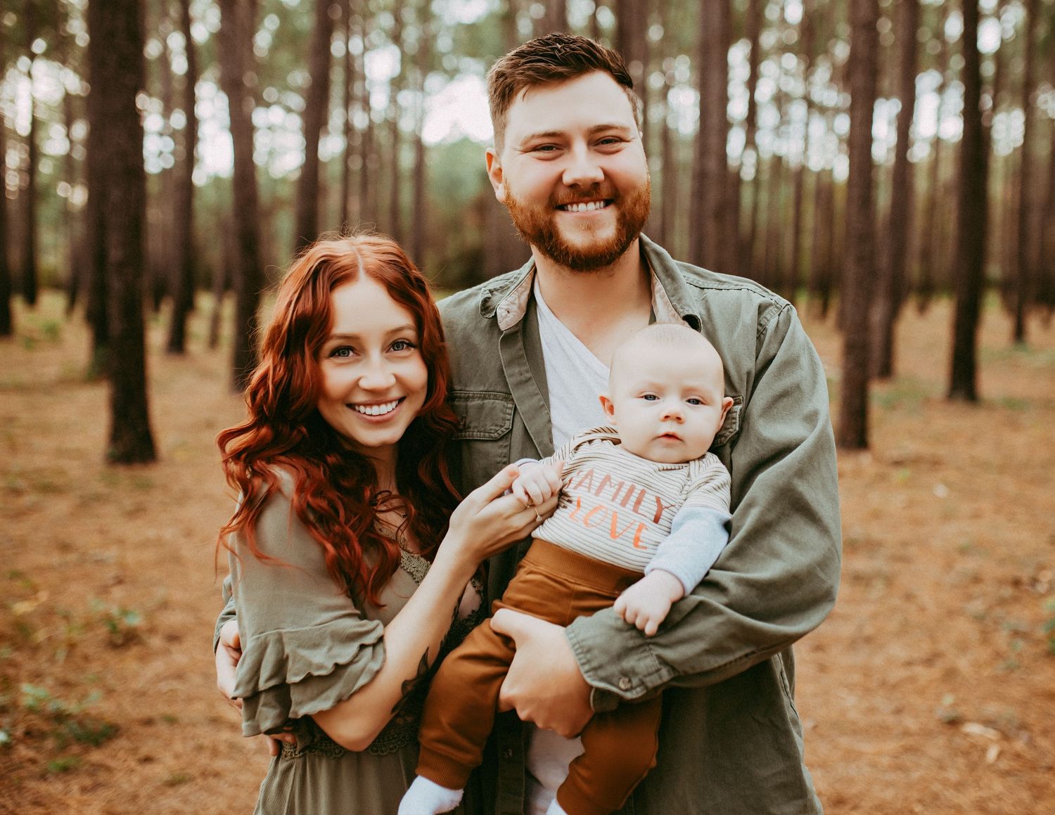 Family in coordinated grey outfits enjoys autumn photoshoot in pine forest setting at sunset.