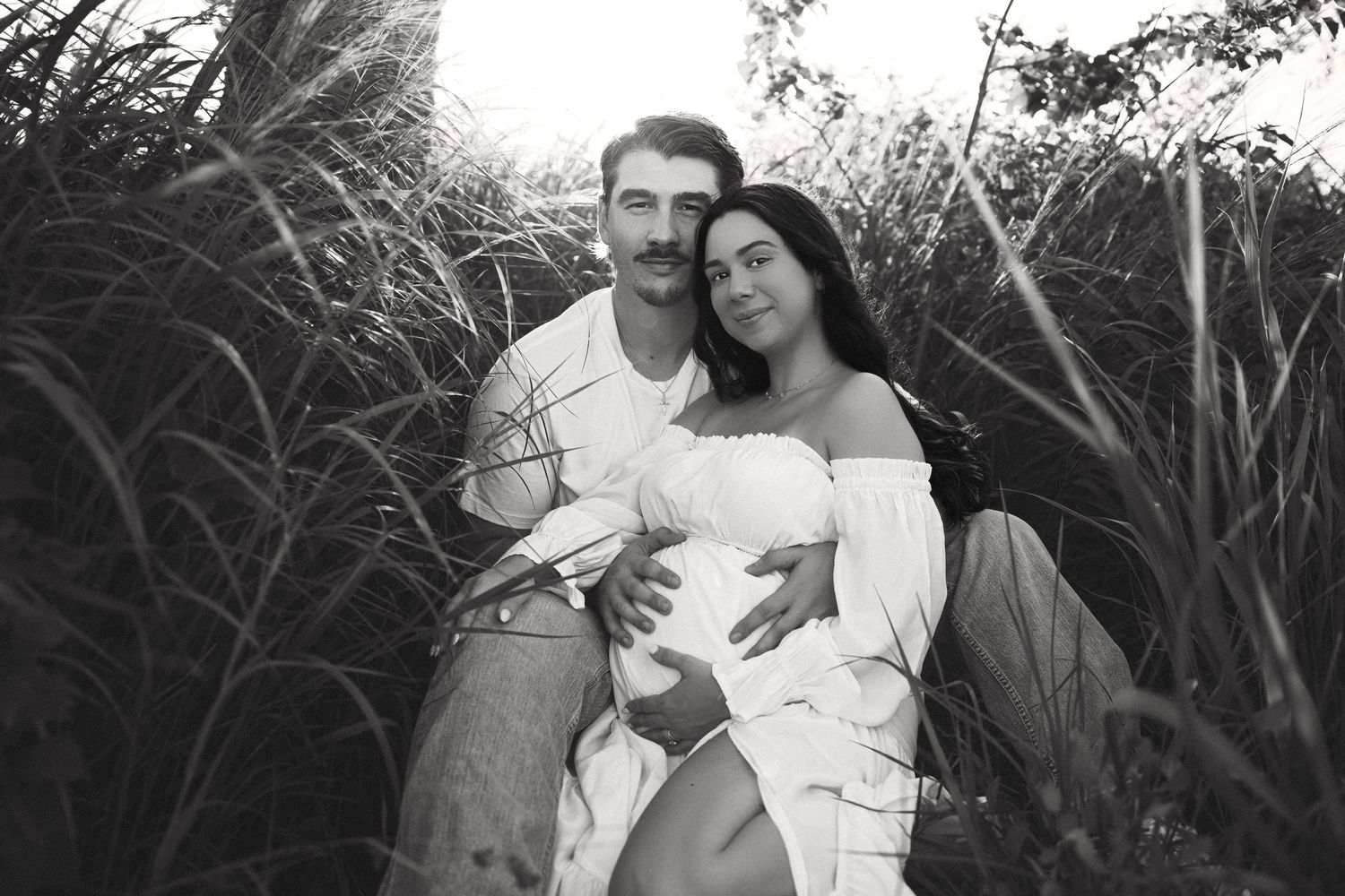 A romantic black and white photo series showing a couple embracing outdoors among tall grass and natural settings.