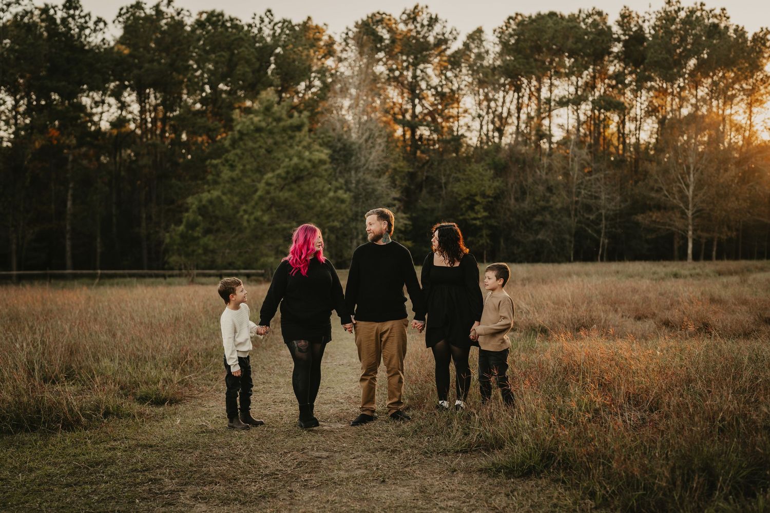 Family of five walking together hand in hand through a golden field at sunset.