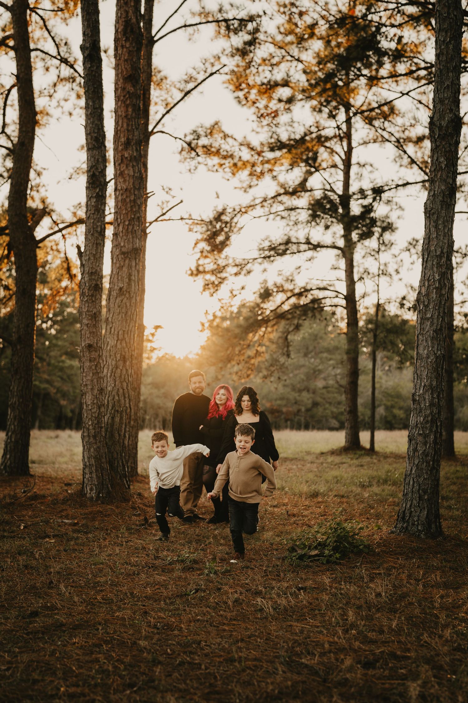 Family group runs playfully through a forest of tall pine trees at golden hour.