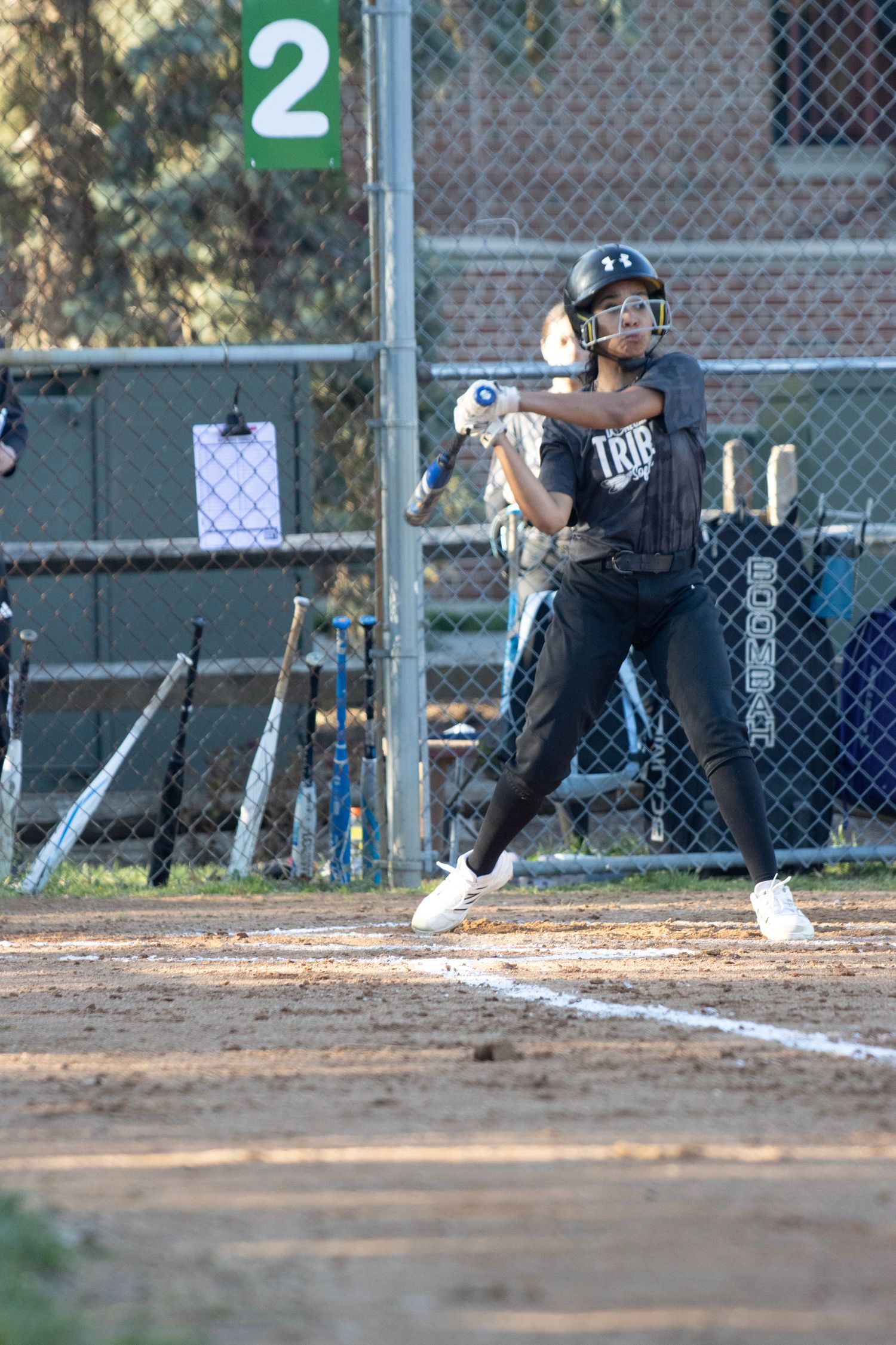 A softball player is standing at the home plate, right after hitting the ball.