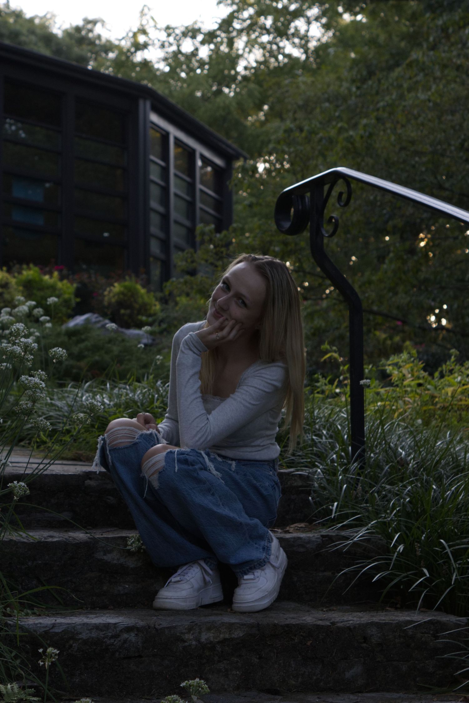 A young woman in a plain white shirt sits on a step, gazing curiously to the left of the frame.