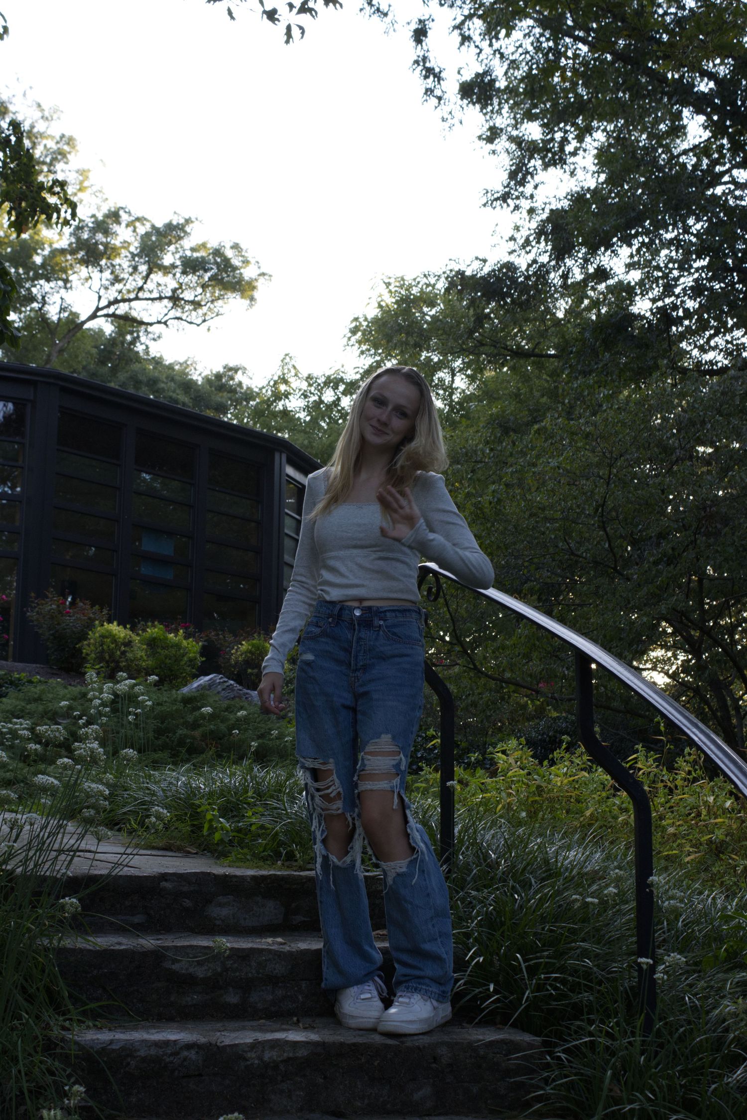 A young woman, standing on a set of stairs, is gazing directly at the camera.