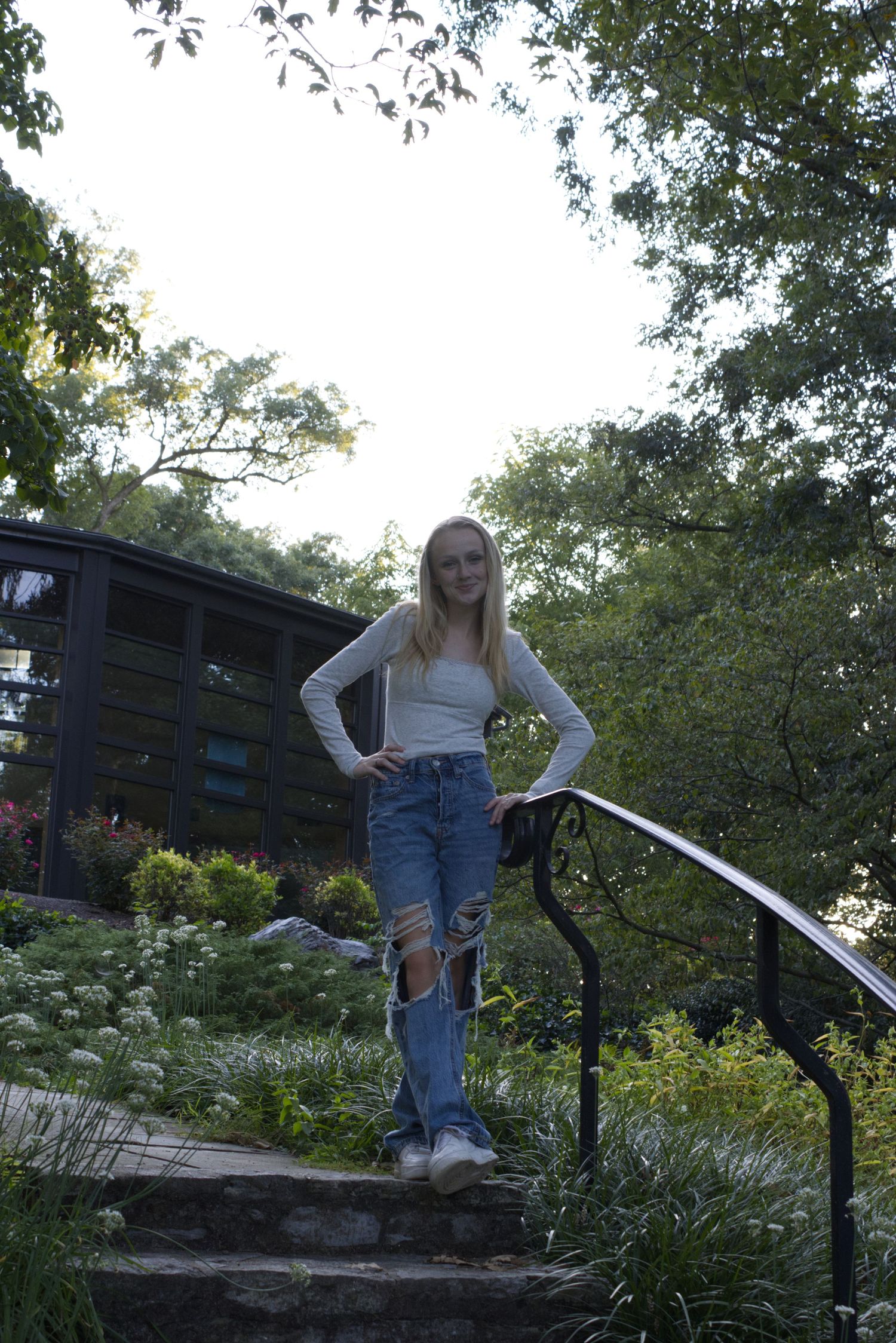 A young woman, standing on a set of stairs, gazes directly at the camera with her hands resting on her hips.